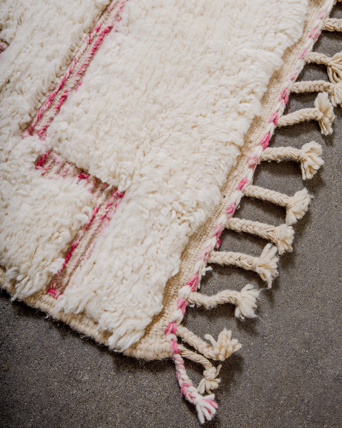 Corner of Berber rug with cream and pink wool and natural wool tassels. 