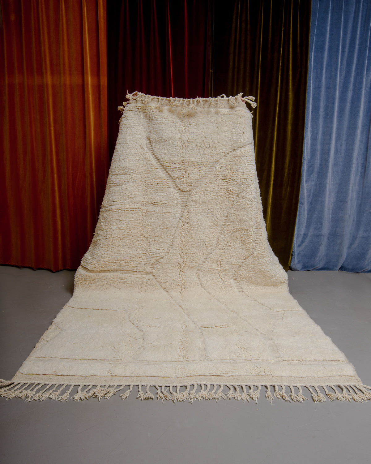 Berberlin Beniourain rug in cream wool with organic line pattern being held up in front of velvet curtains.