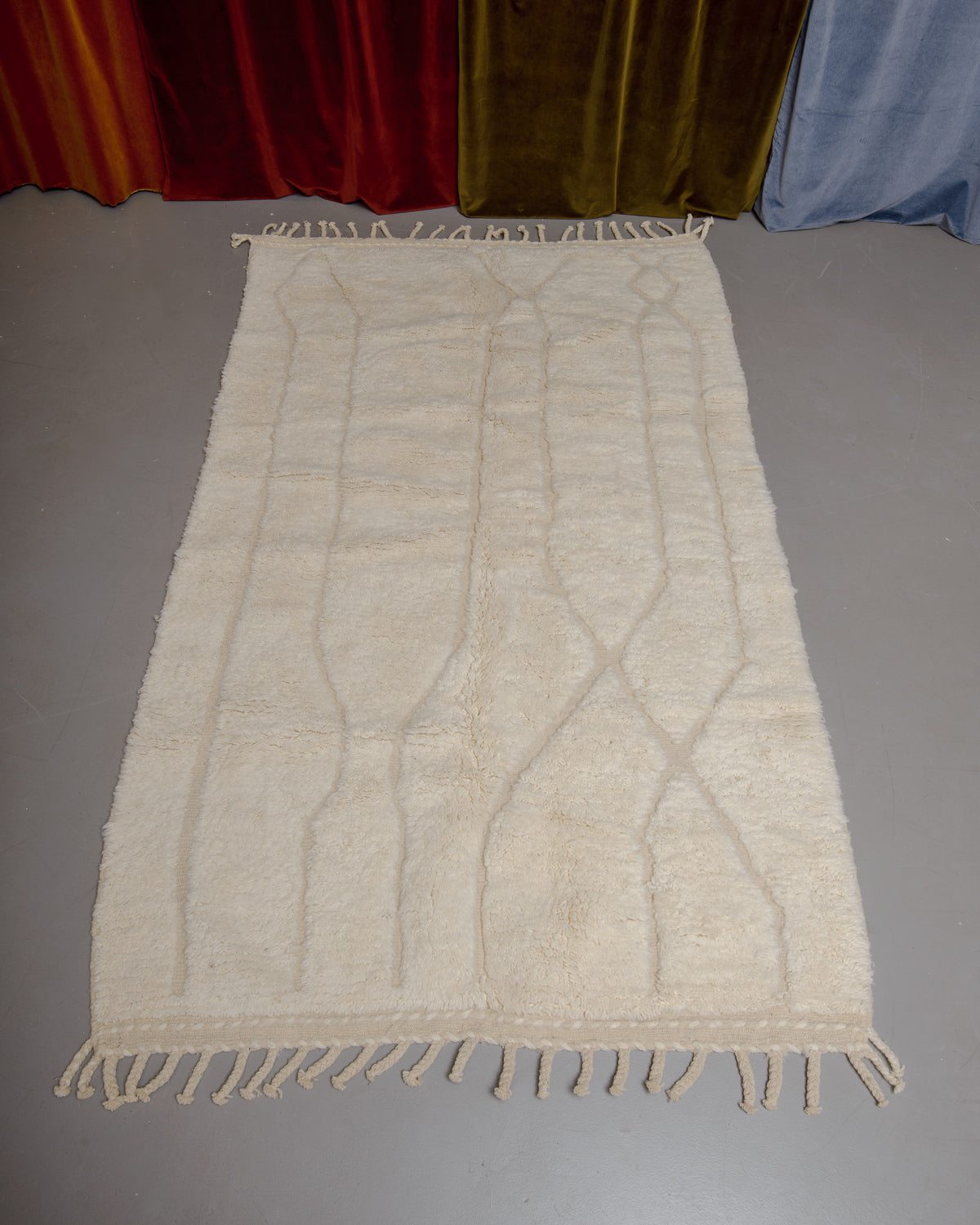 Berberlin Beniourain rug in cream and wool on grey floor in front of velvet curtains.