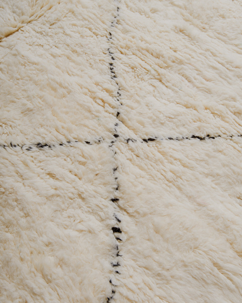 Close up of surface of cream wool rug with black lines.