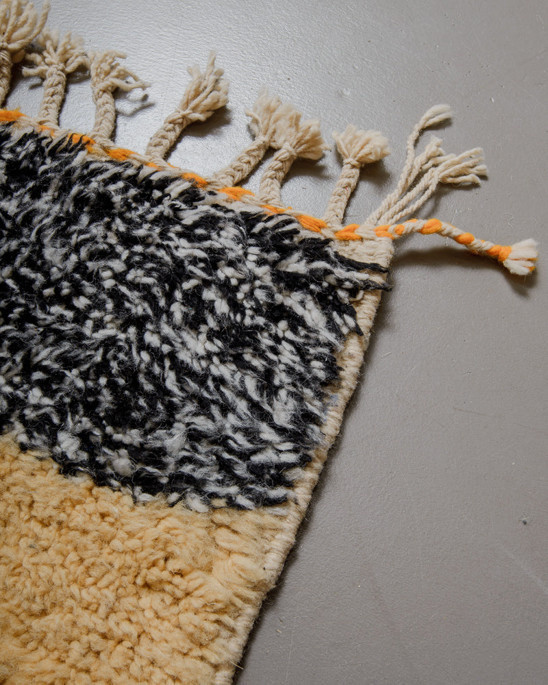 Corner of wool rug with tassels on grey floor. 
