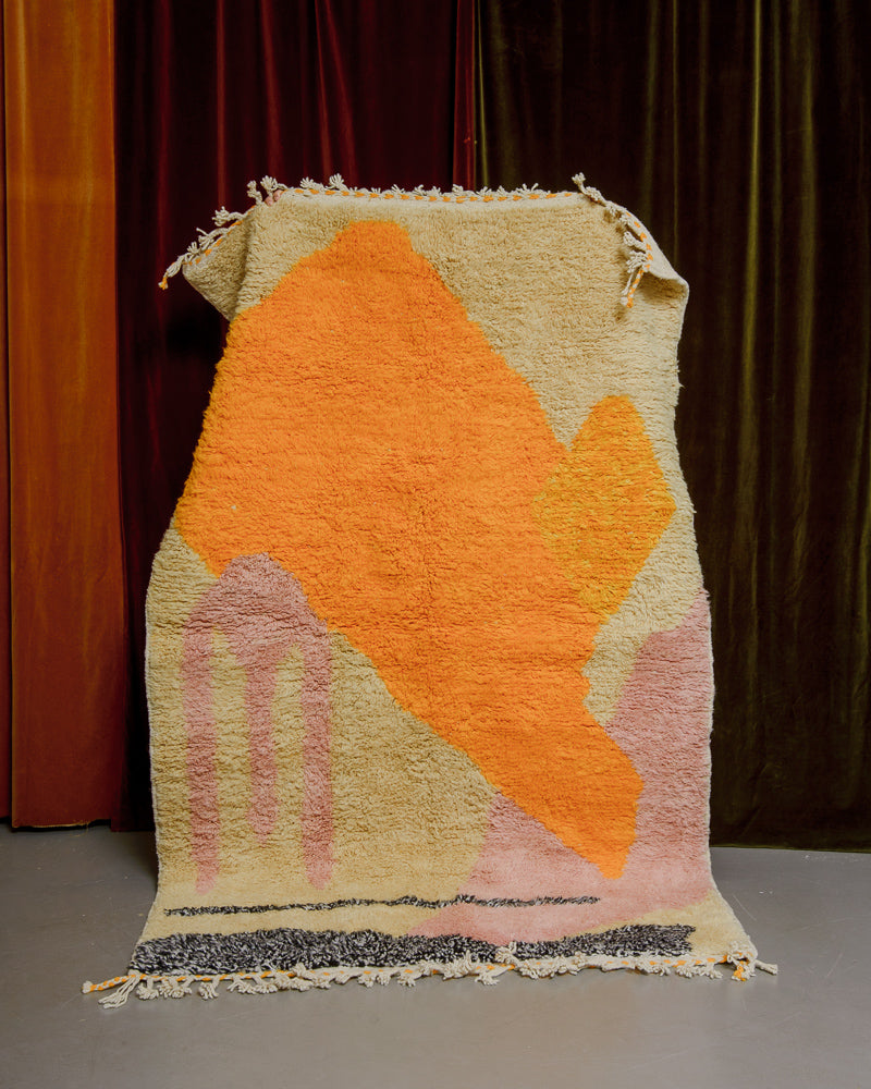 Colourful Berberlin rug being held up in front of velvet curtains. 