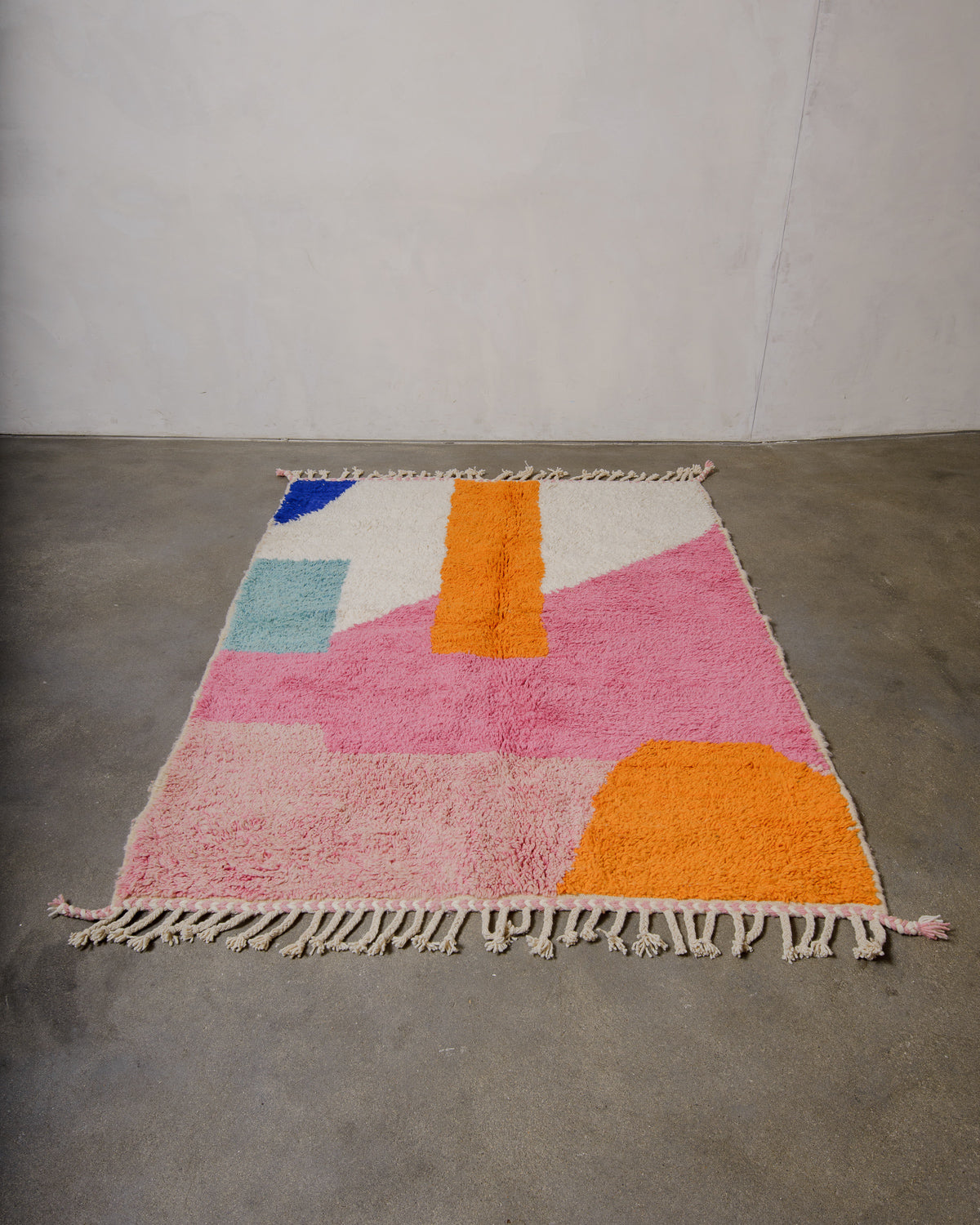 Berberlin beniourain rug in bold shades of pink, orange and blue laying on a concrete floor. 