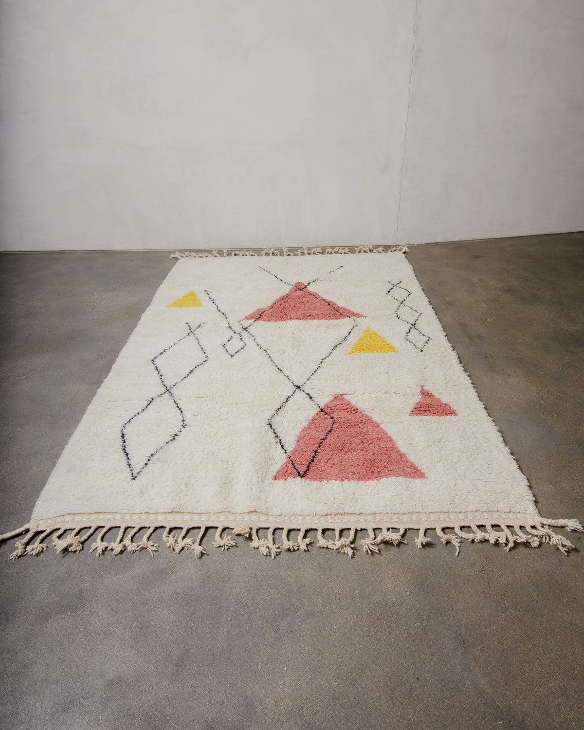 Cream rug with abstract geometric design  laying on concrete floor.