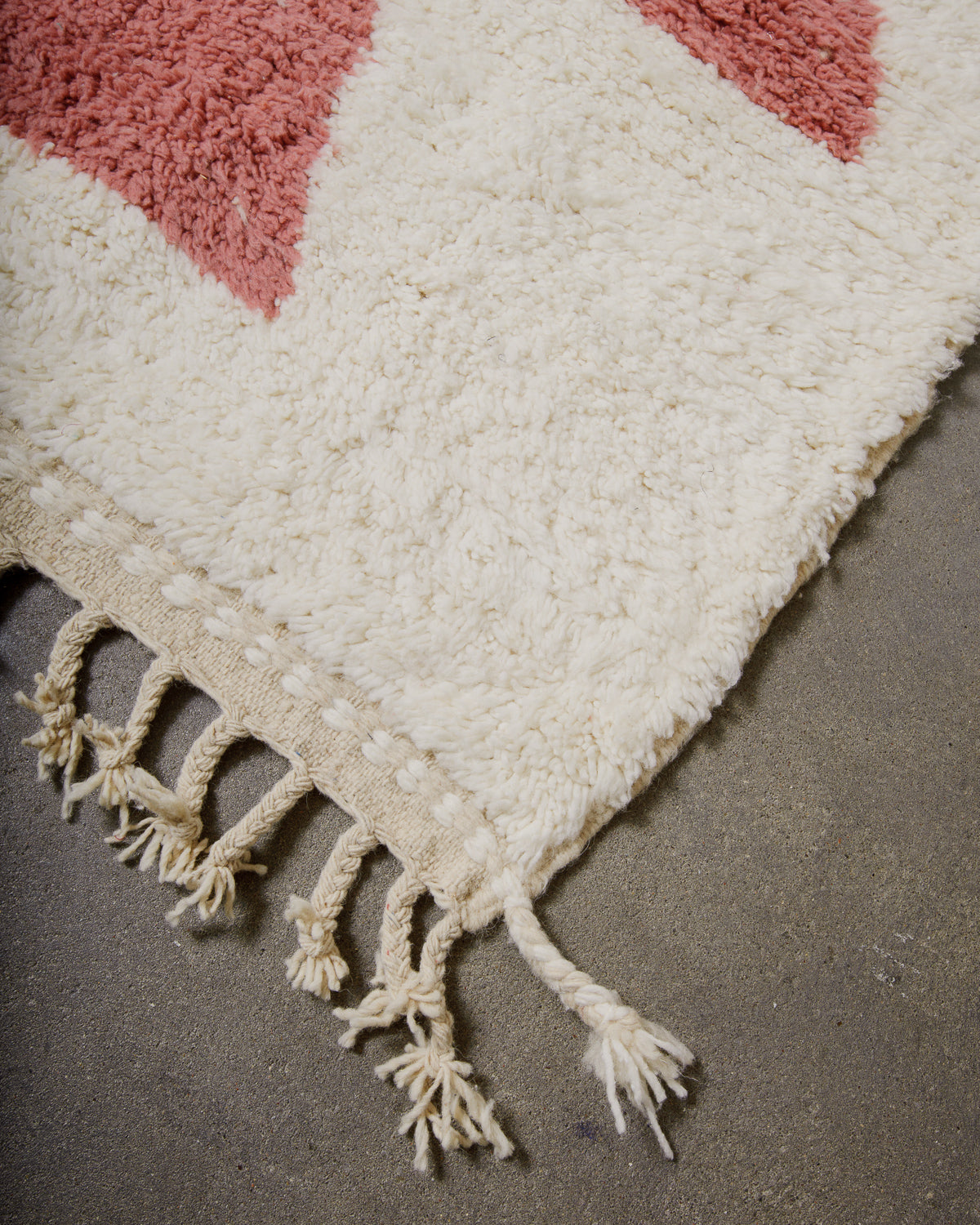Corner of wool rug with tassels on concrete floor. 
