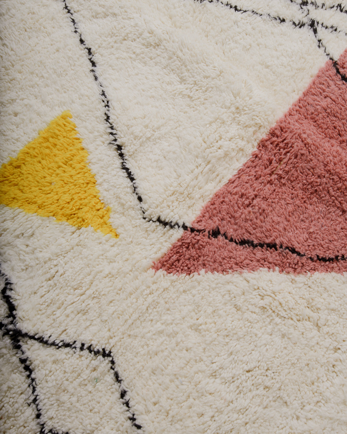 Close up of surface of wool rug with triangle elements in pink and yellow. 