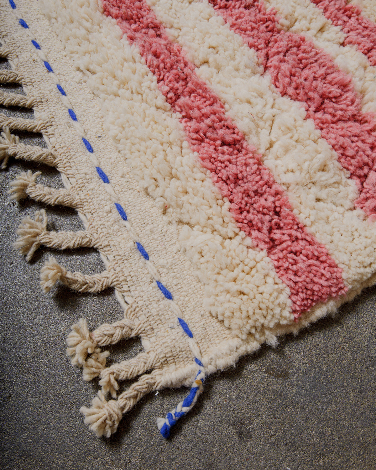 Corner of wool rug with pink and cream stripes and blue details in the woven end.