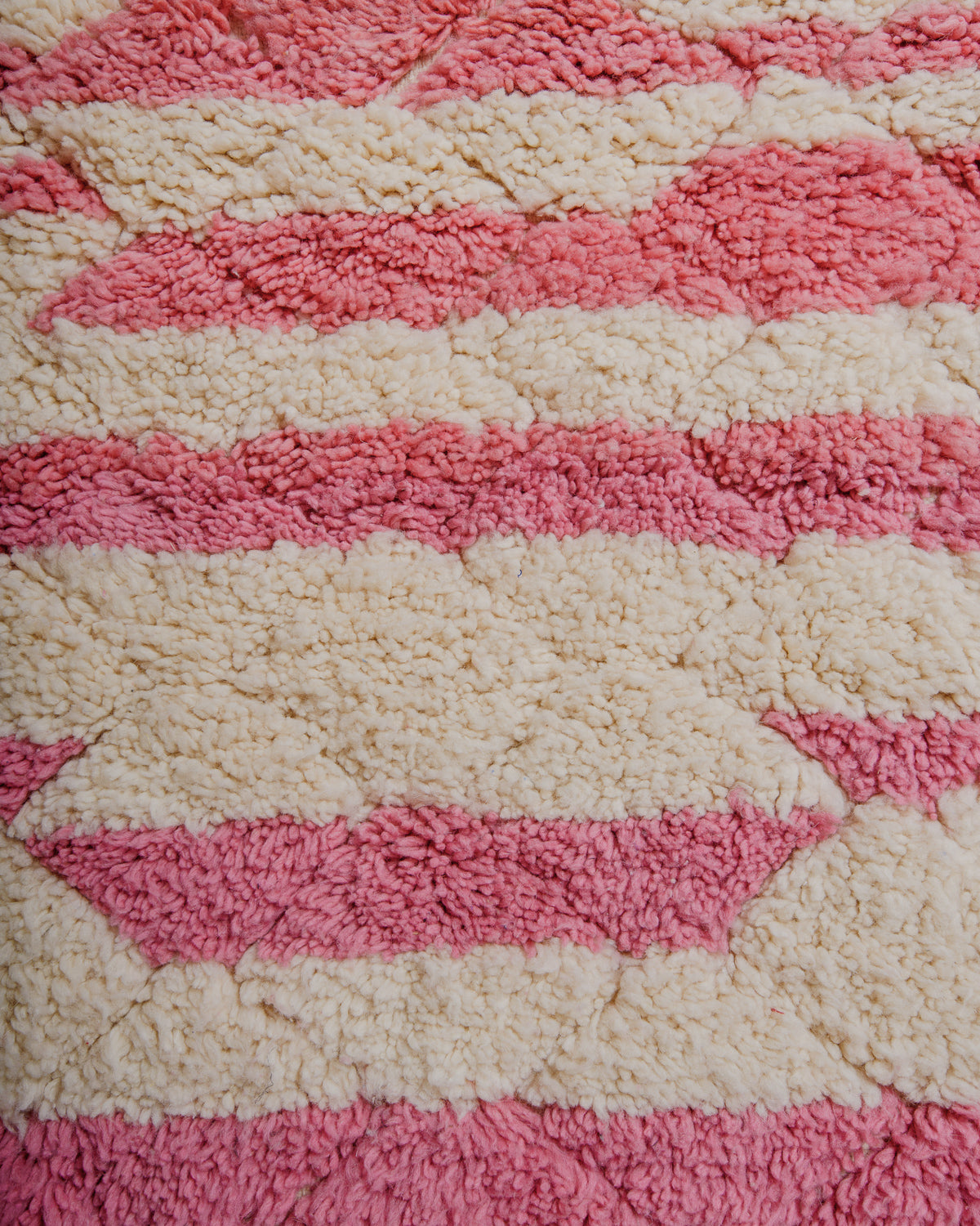 Surface of wool rug in pink and cream stripes with subtle lattice pattern.