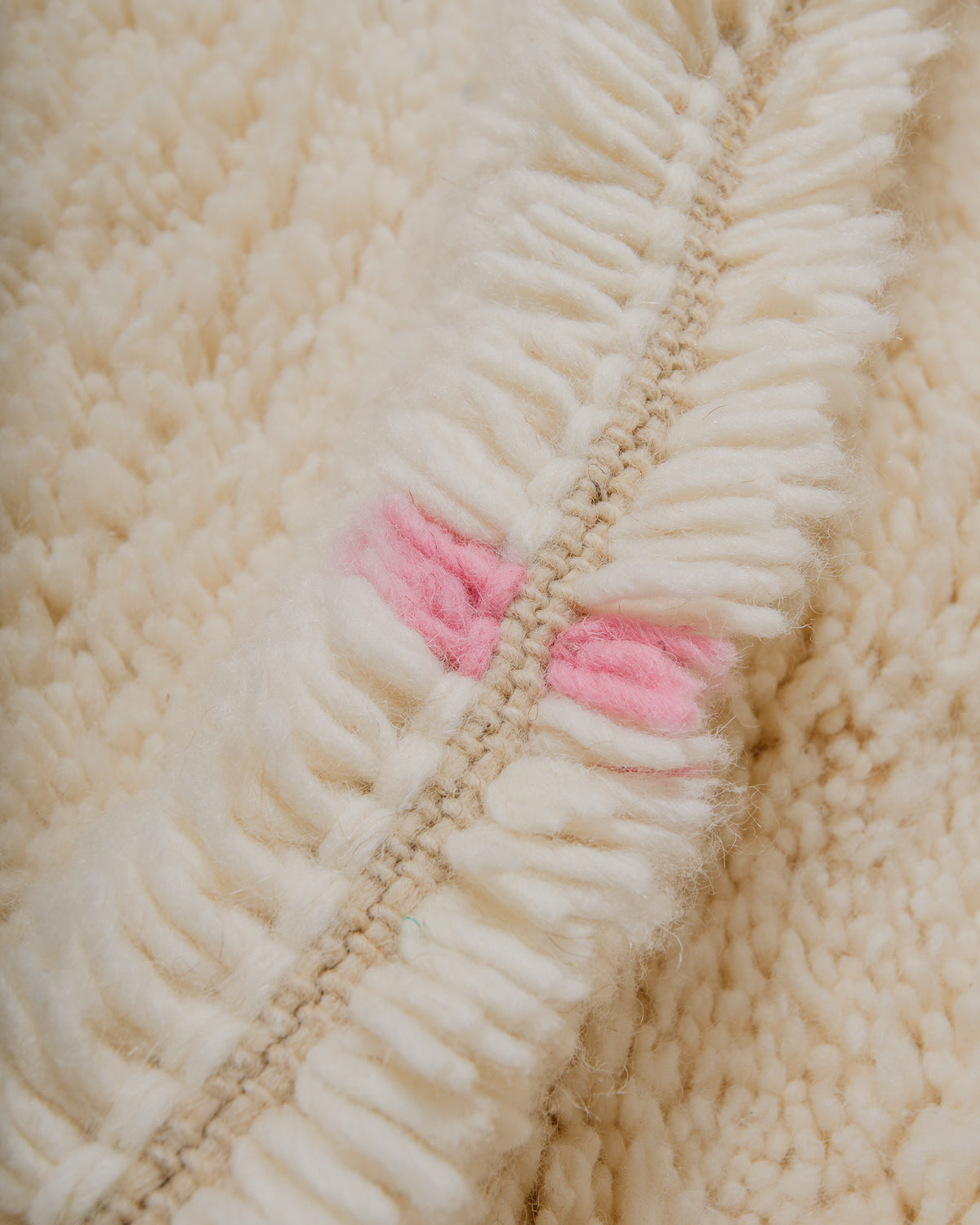 Close up of cream wool rug with pink wool detail.