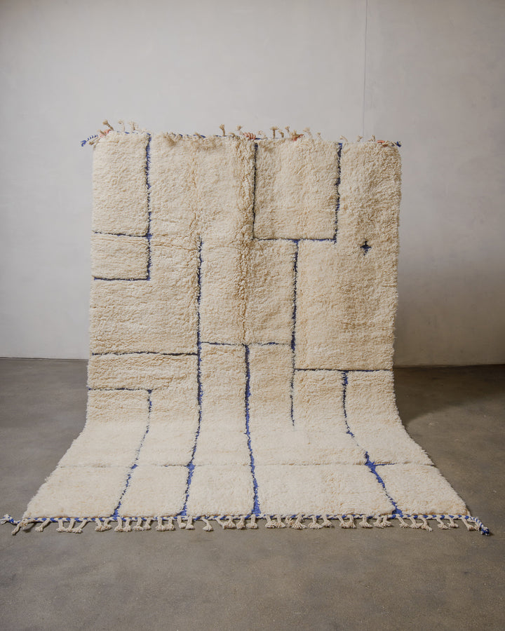 Beige and blue geometric patterned rug on a plain floor with a neutral wall background