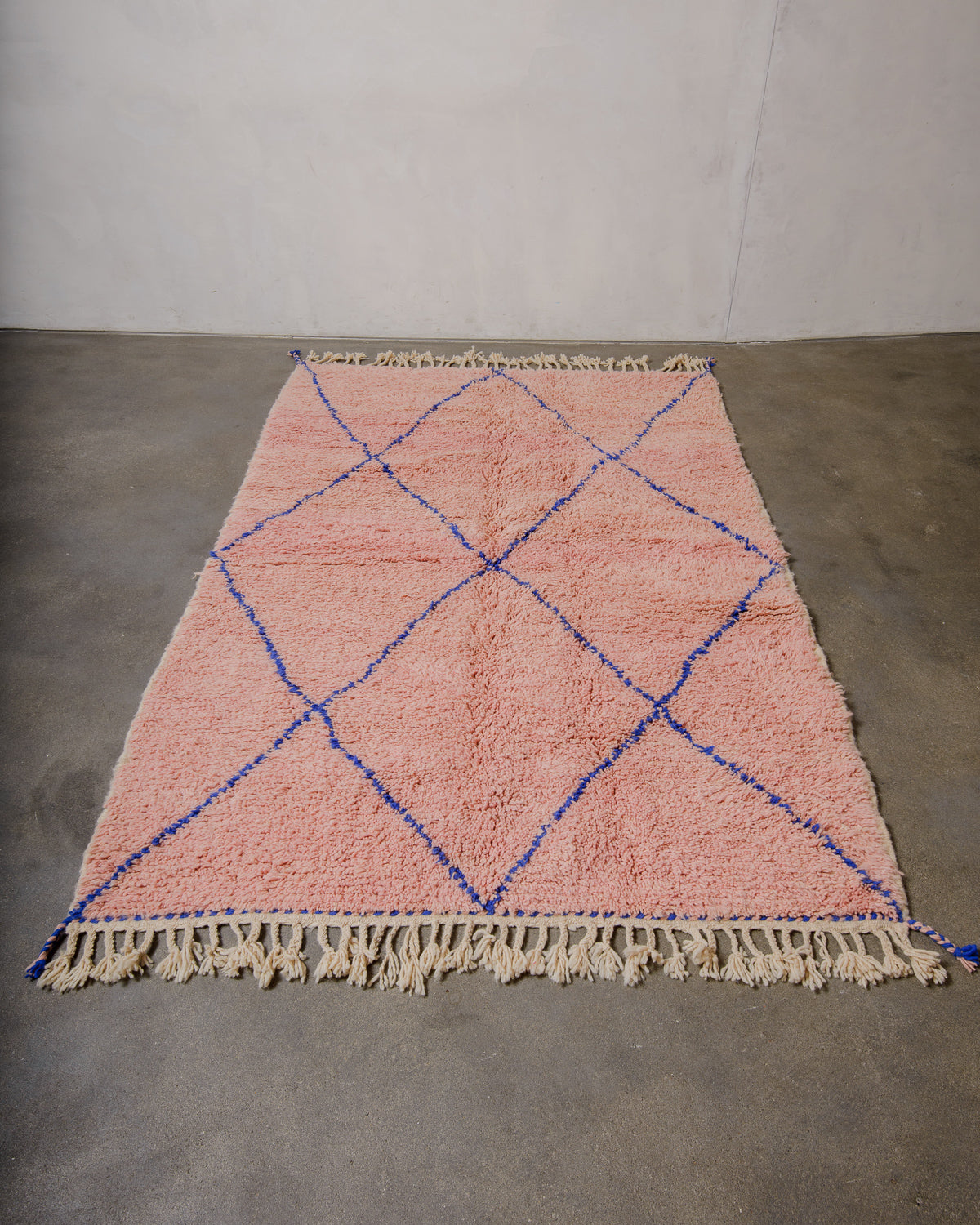 Berberlin beniourain in soft rose with a dark blue diamond pattern laying on a concrete floor.
