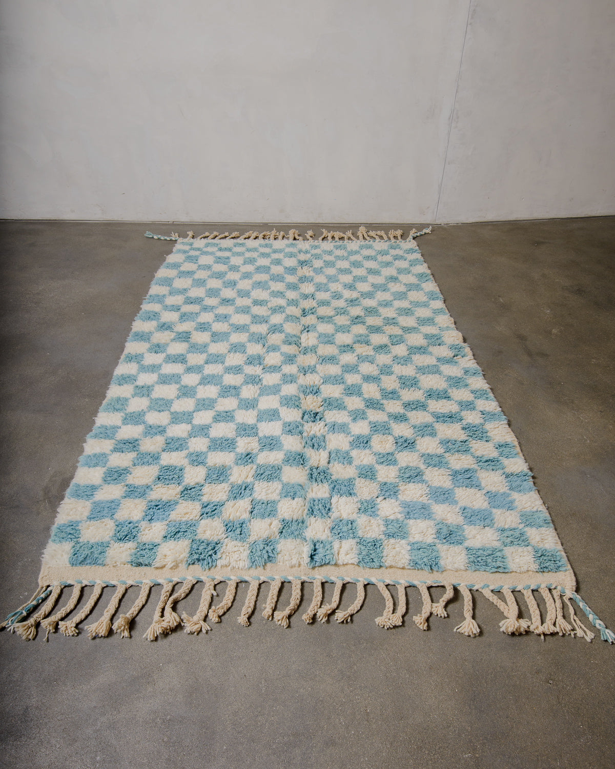 Berberlin beniourain rug in cream and blue checkered pattern laying flat on concrete floor. 