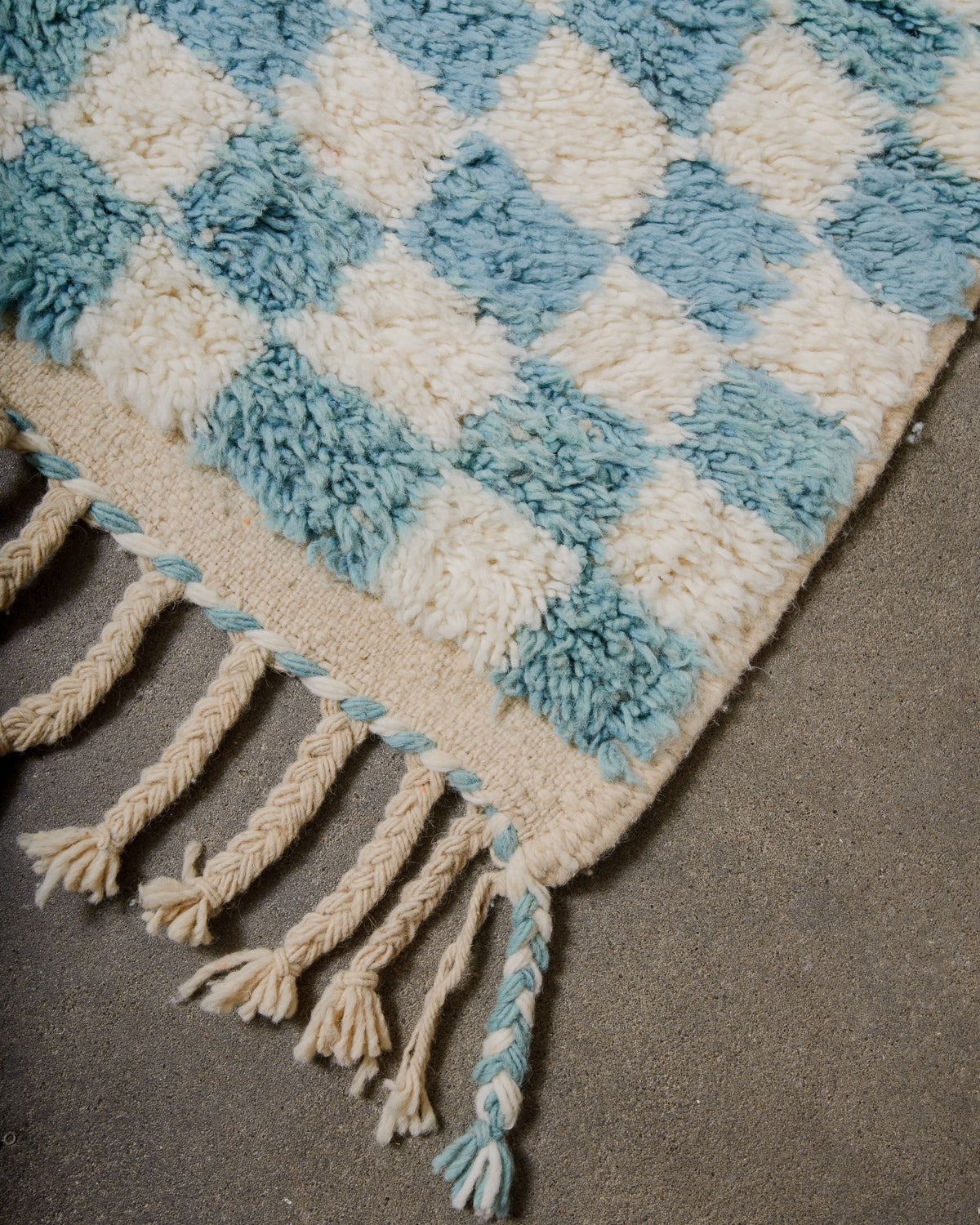 Checkered wool rug with tassels on concrete floor .