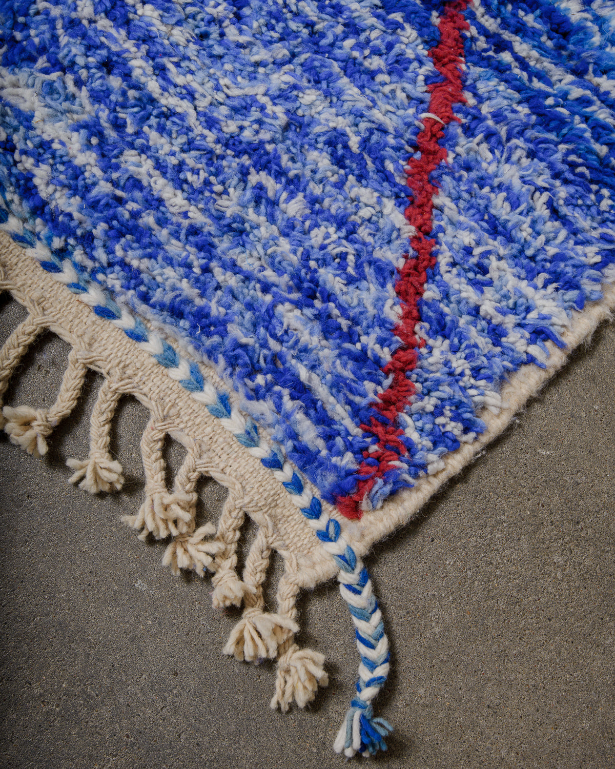 Corner of blue wool rug with natural wool tassels on concrete floor. 