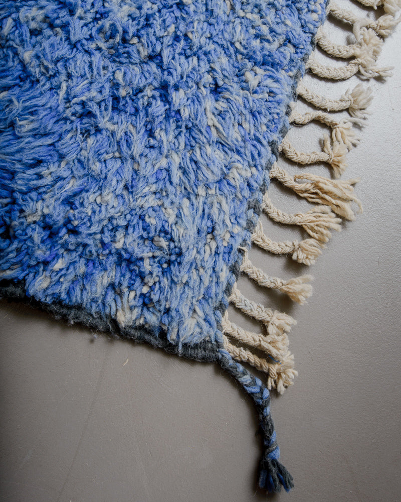 Corner of blue wool rug with natural wool tassels. 