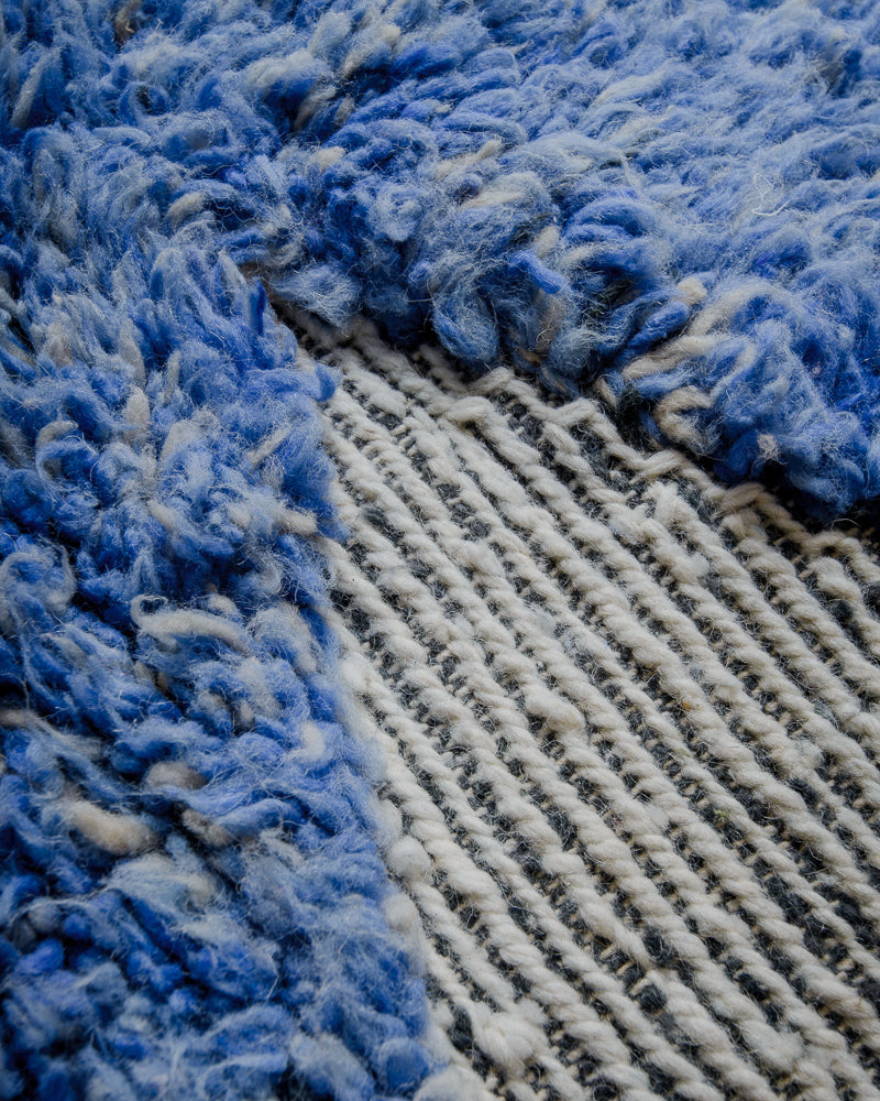 Close up of wool rug with thick blue pile and woven areas in grey and white. 