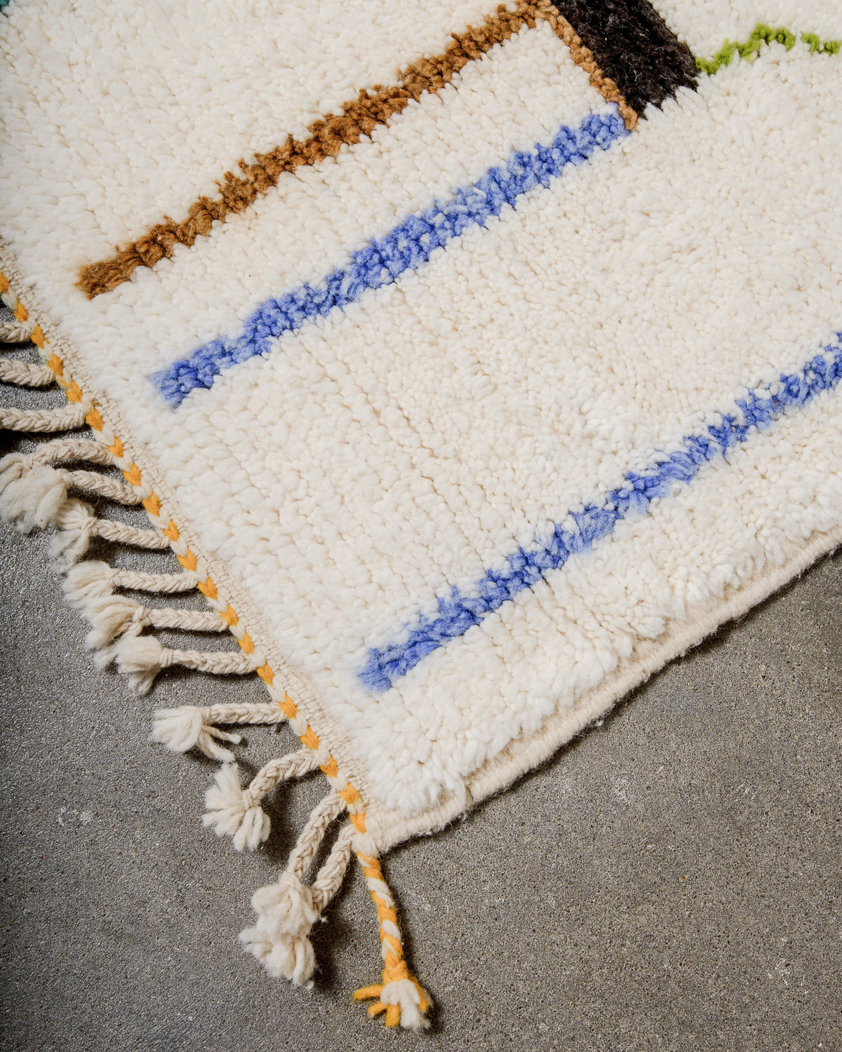 Corner of cream berber rug that is finished with tightly woven ends with yellow and cream trim.