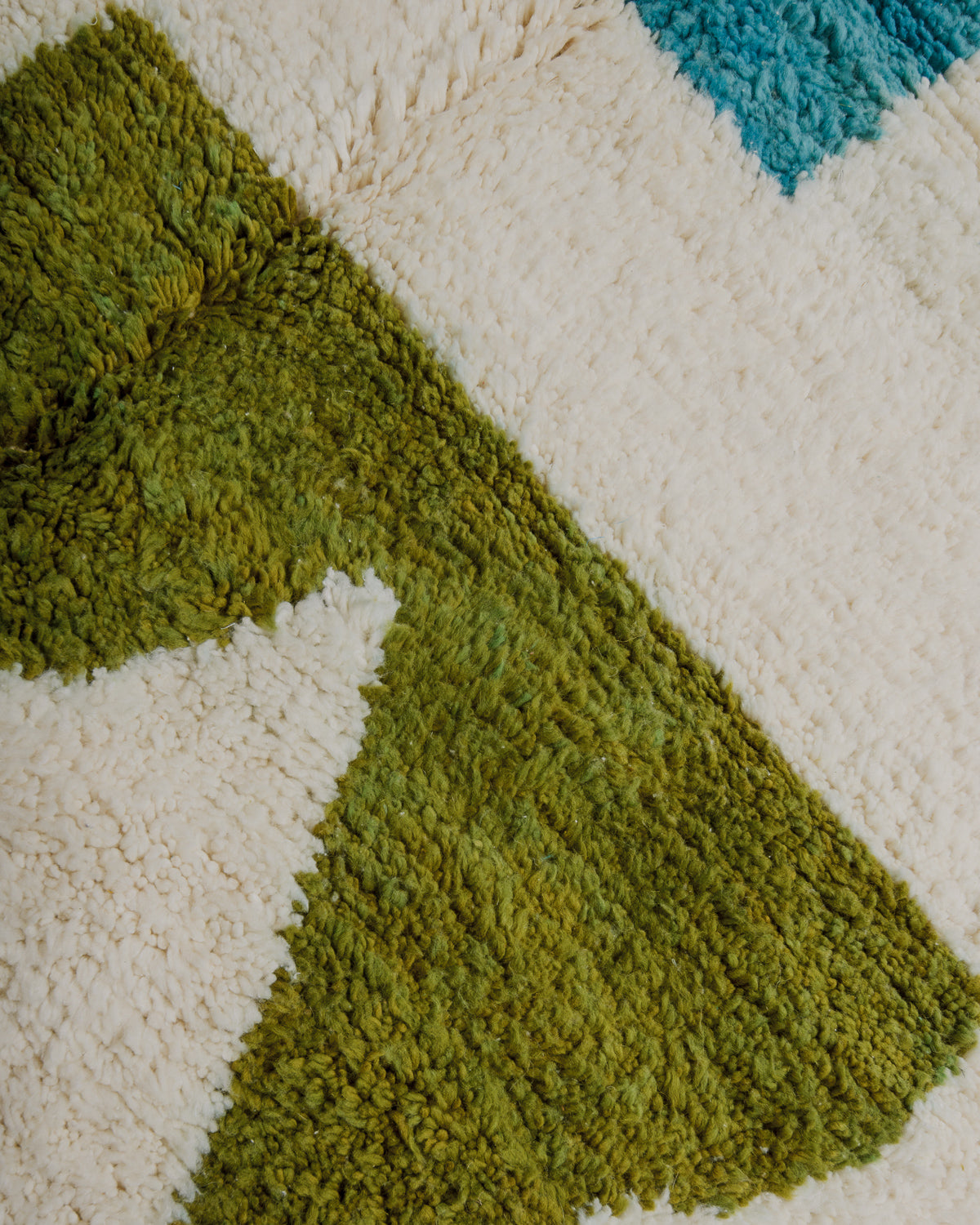 Close-up of a textured rug with green, blue, and cream colours.