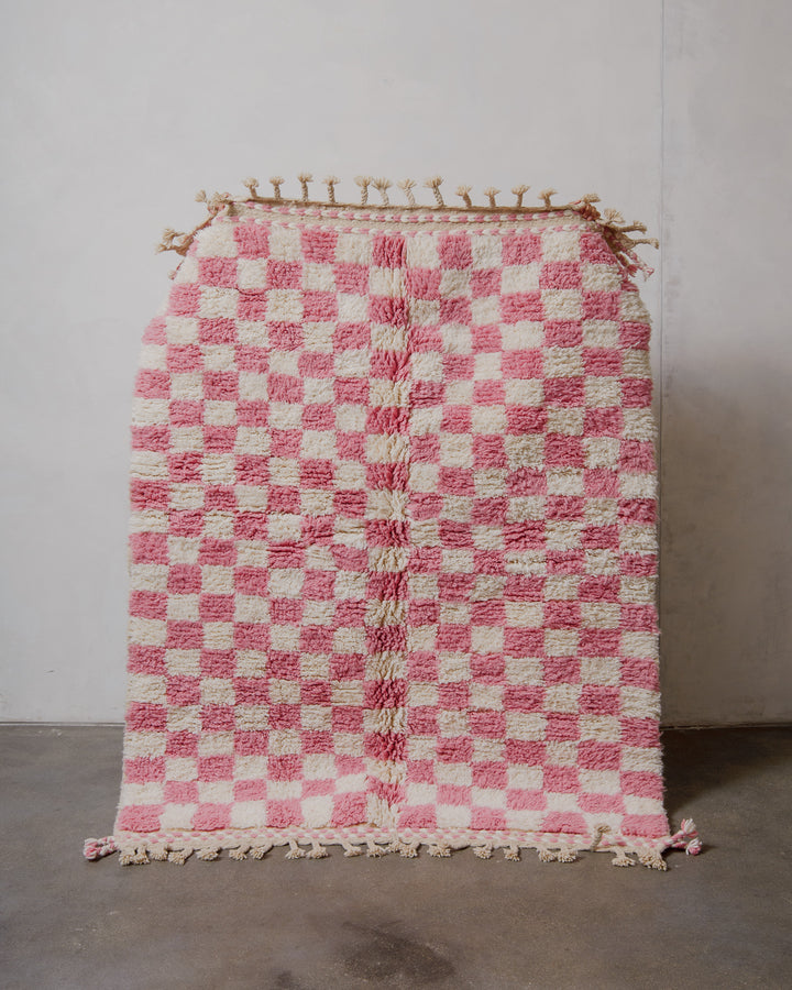 Pink and white checkered rug with tassels on a plain background