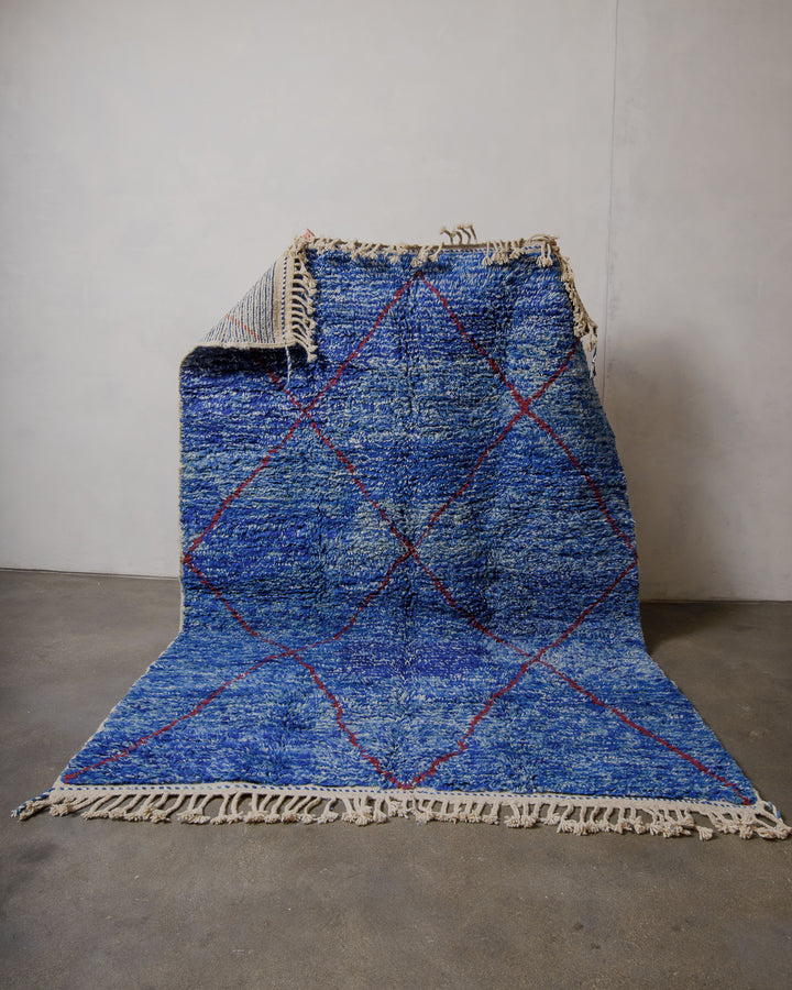 Berberlin special edition rug in blue being held up in front of a plain wall. 