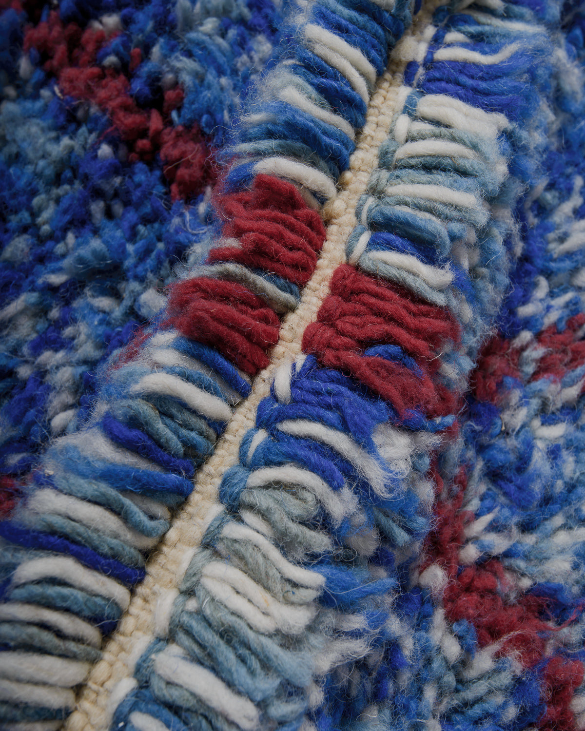 Close up of speckled blue rug with maroon details. 