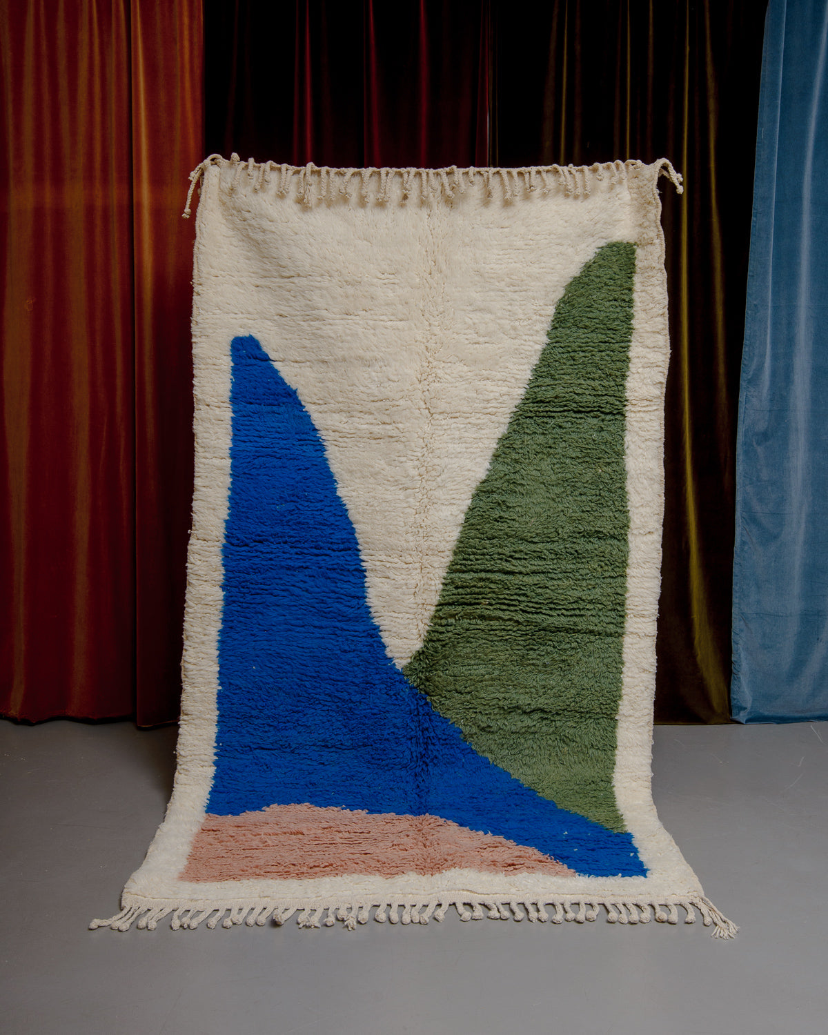 Berberlin beniouran rug in cream with colourful forms being held in front of velvet curtains.