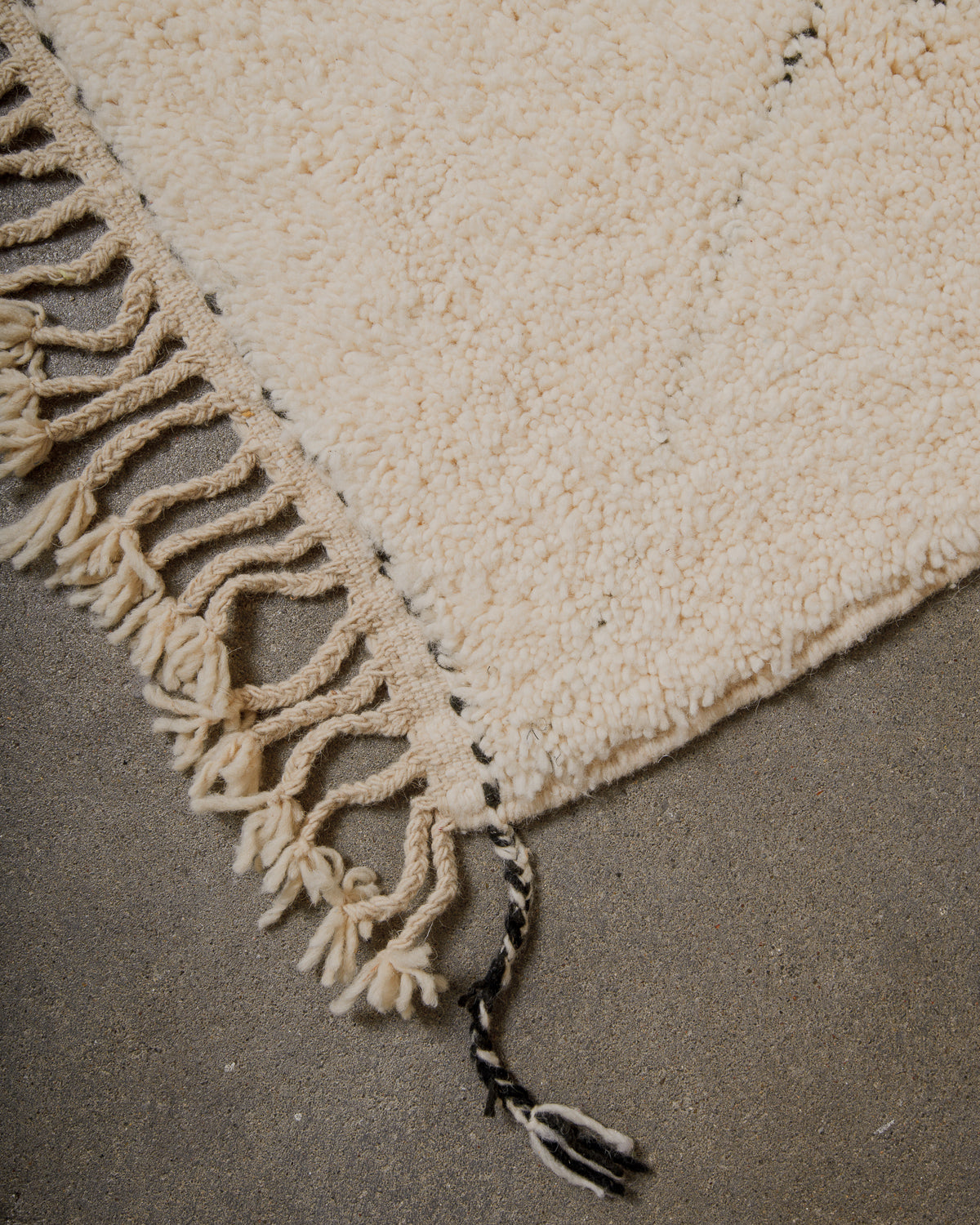 Corner of cream rug with natural wool tassels and black and white corner tassel. 
