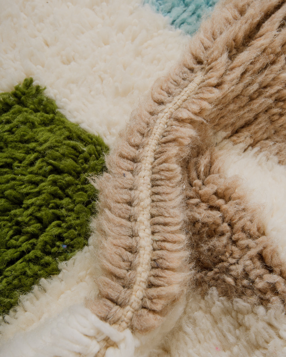 Close-up of fluffy wool rug with green, beige, and cream.