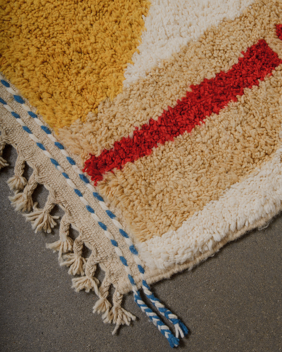 Close-up of a textured rug with geometric pattern and tassels on a gray surface