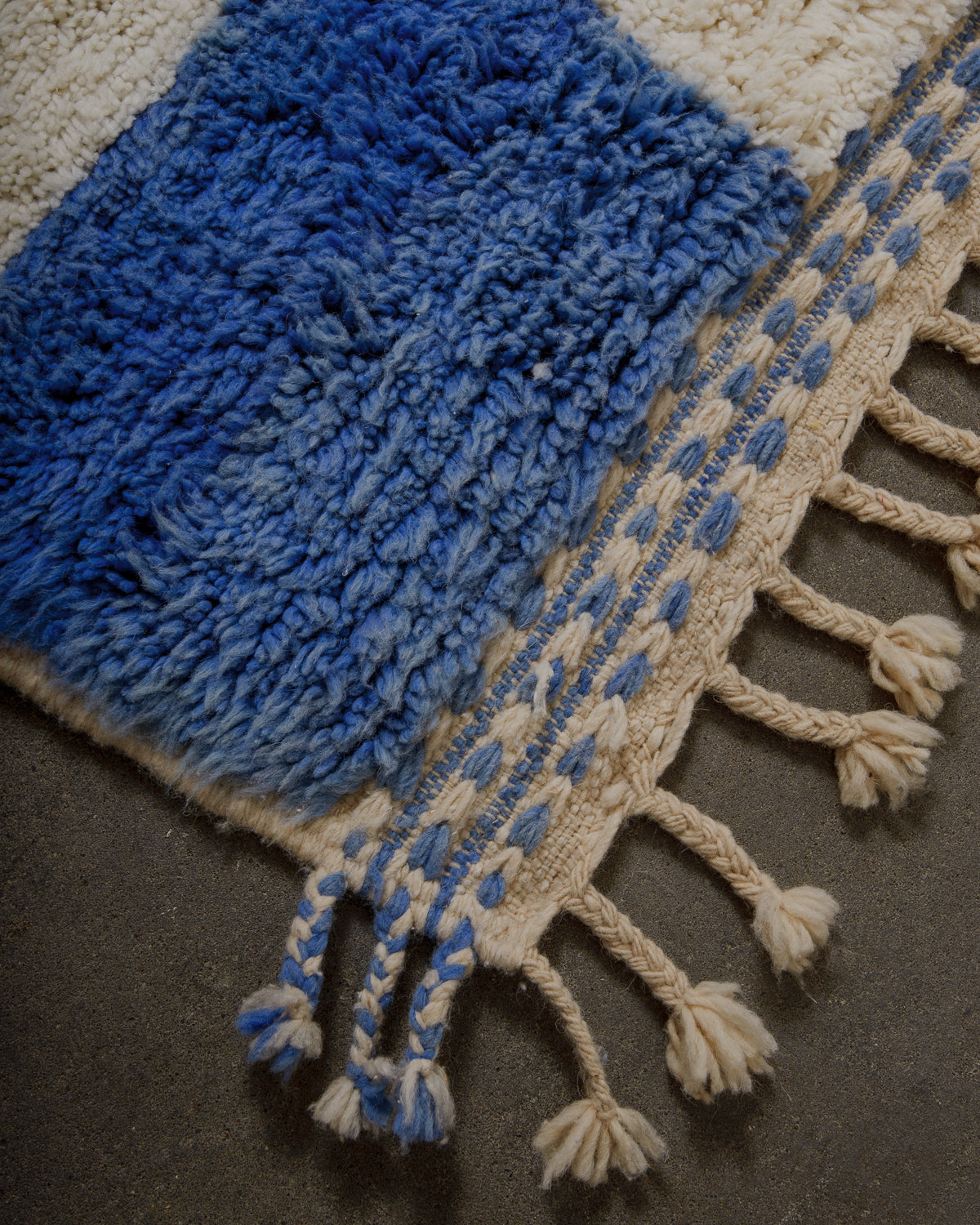 Blue textured rug with tassels on a dark surface