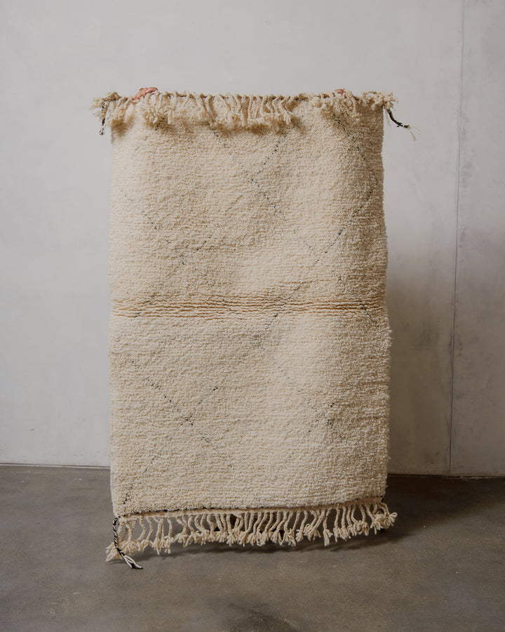 Cream Berberlin Beniourain rug with subtle classic diamond design held in front of a plain wall. 