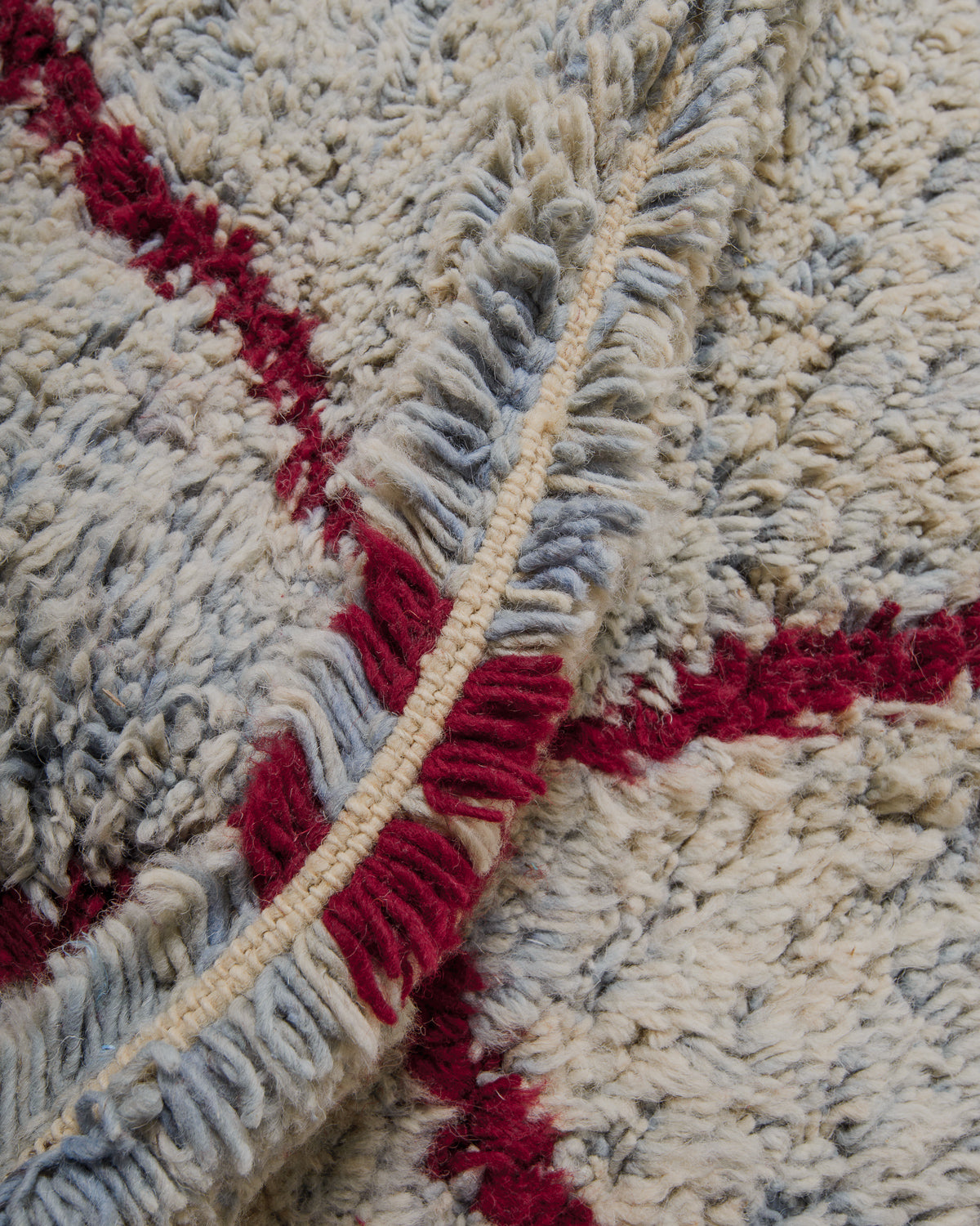 Close up of rug with fluffy speckled blue wool and burgundy lines. 