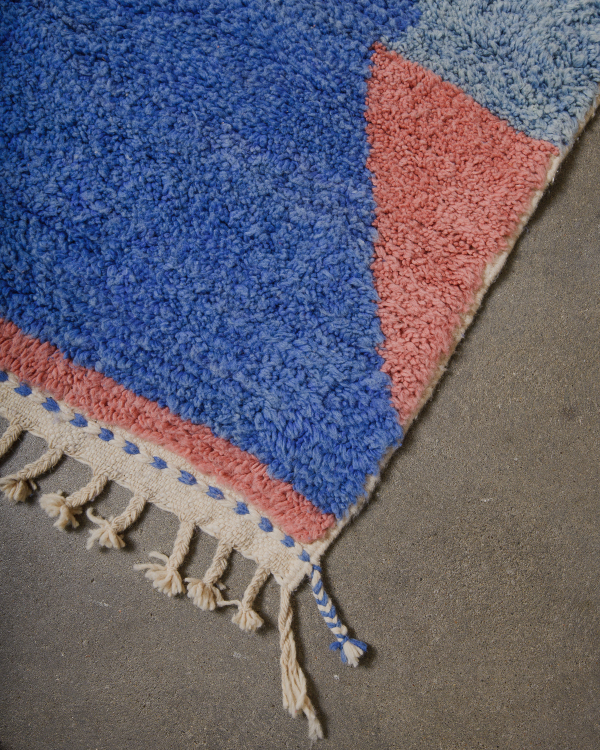 corner of rug featuring cobalt blue, light sky blue and coral rose pink and natural wool tassels.