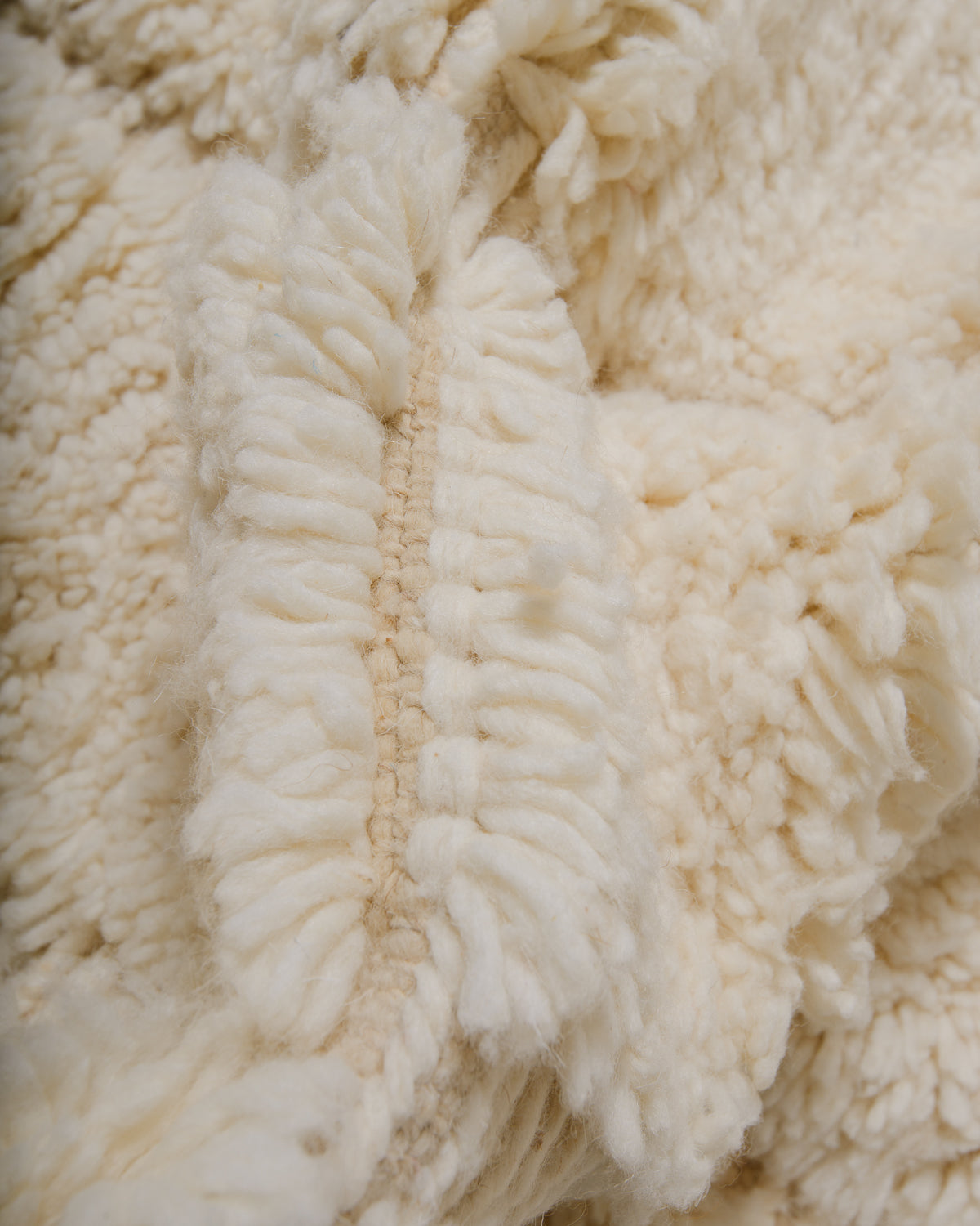 View of weft rows between knotted rows of cream wool rug.