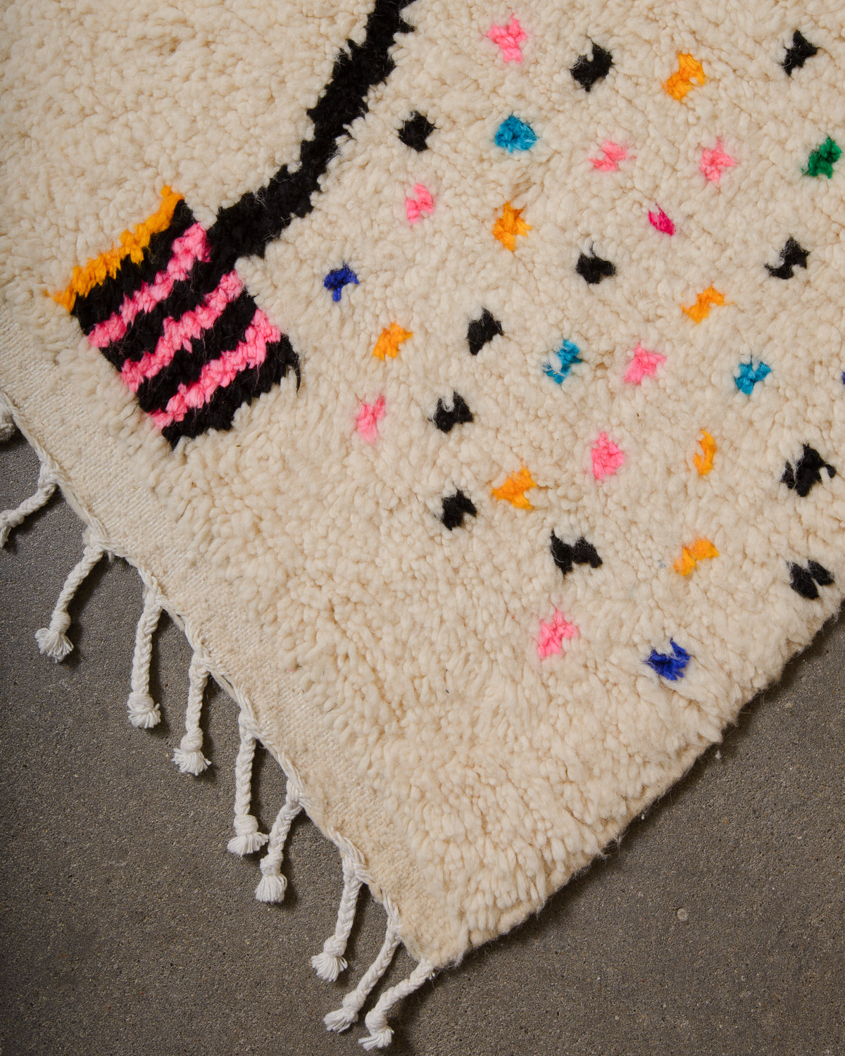 Corner of Azilal run with cream wool and colourful dots and white cotton tassels across the edge.