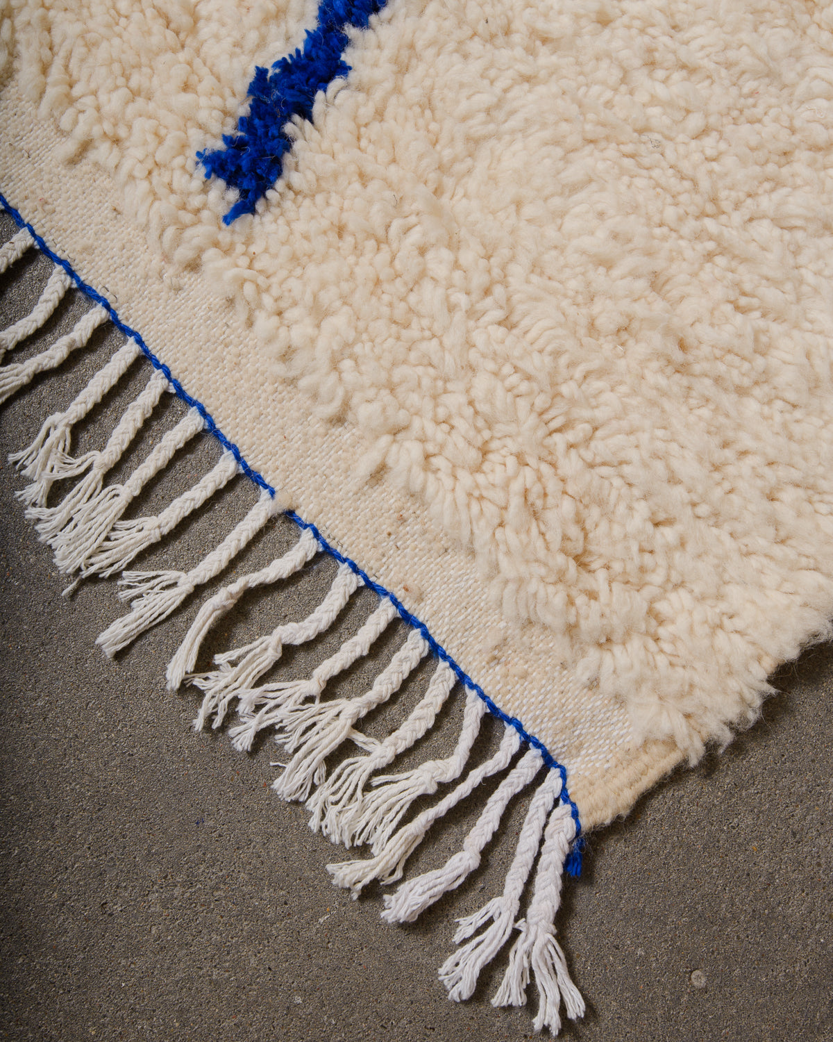 Corner of Azilal run with cream wool and colourful design and white cotton tassels across the edge with blue trim.
