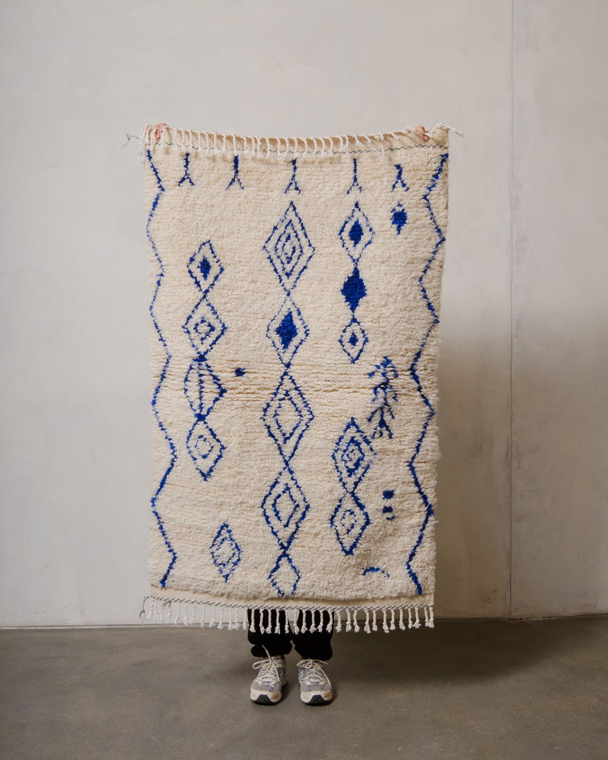 Berberlin Azilal rug in cream wool with blue cotton  being held up in front of a white wall.