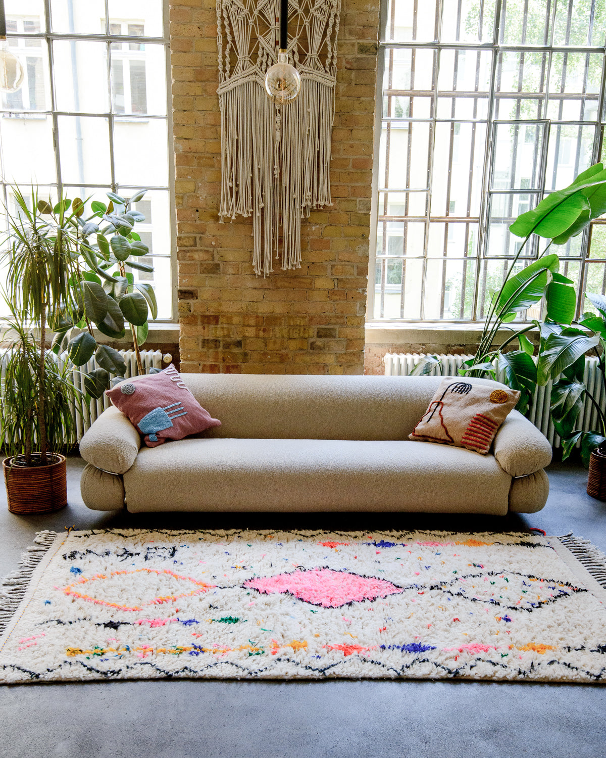 An Azilal rug lies on the floor in front of a cream couch and high warehouse windows.