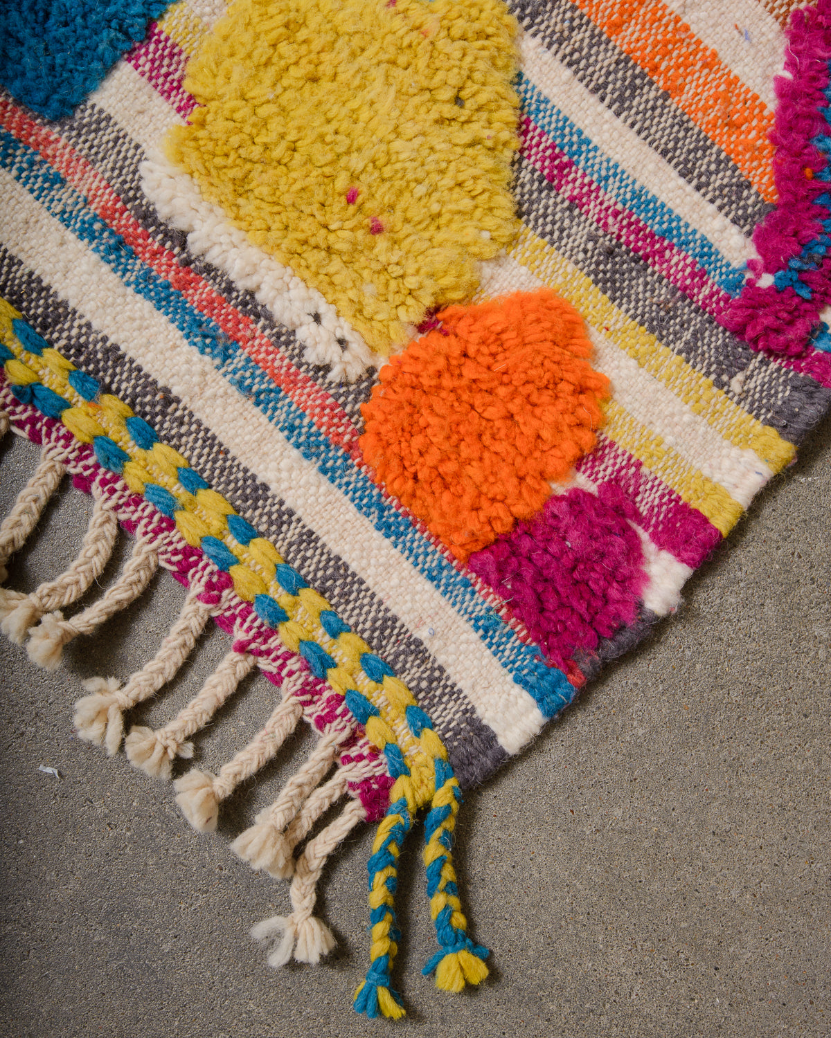 Corner of wool berber rug that is finished with tightly woven ends and natural wool tassels across the ends.