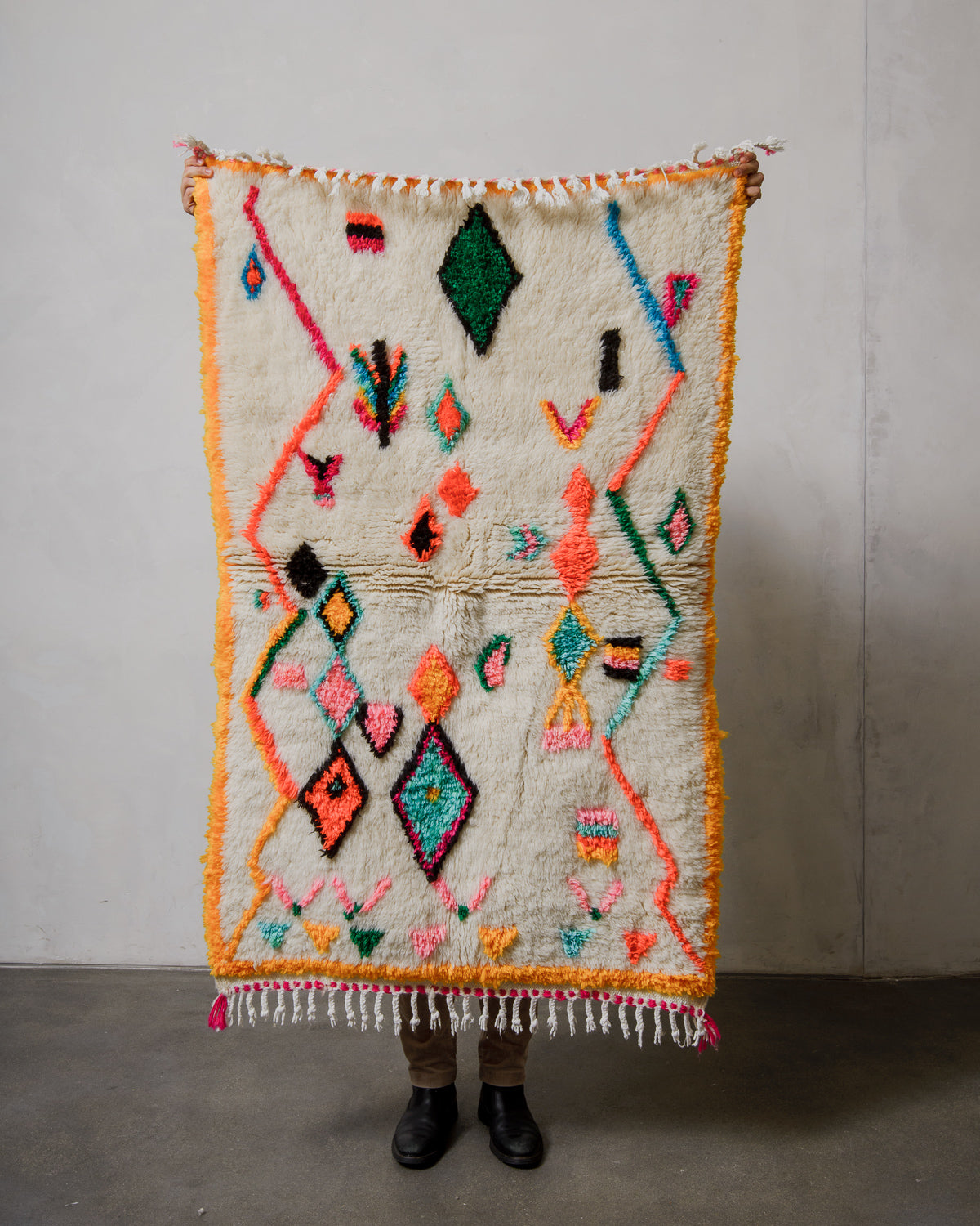 Berberlin Finest azilal rug with colorful patterns held by a person against a plain wall.