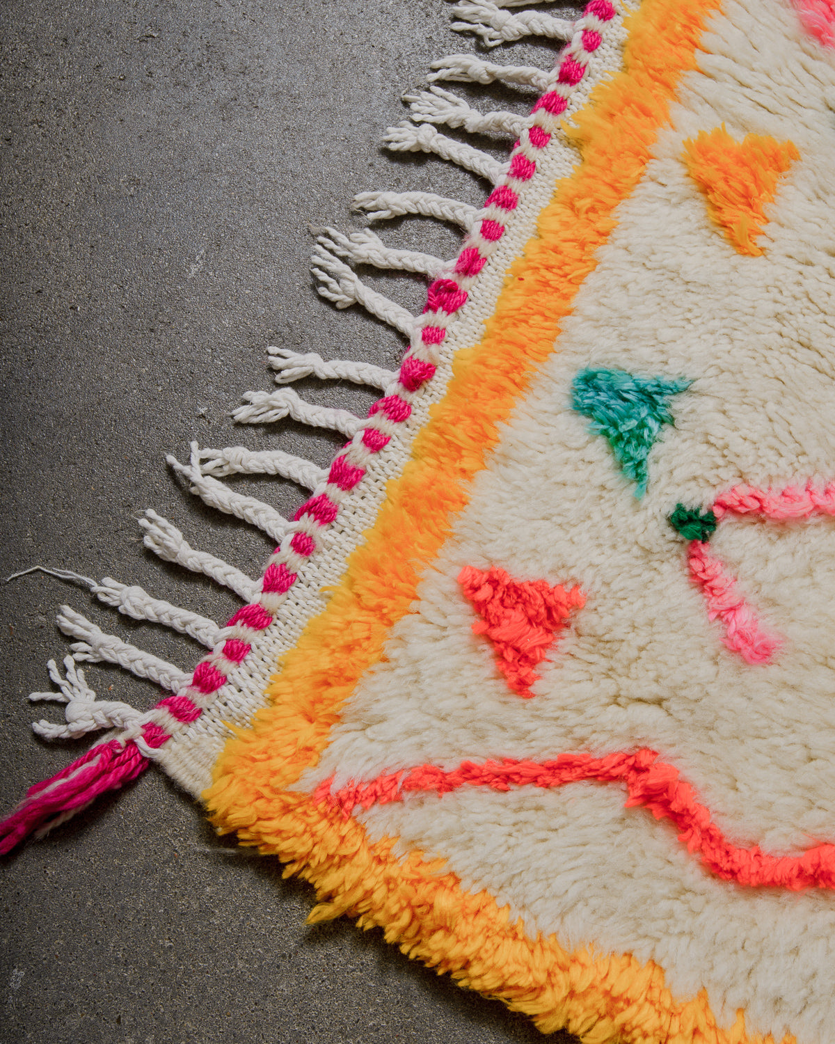 Corner of rug with yellow border and white cotton tassels on concrete floor. 