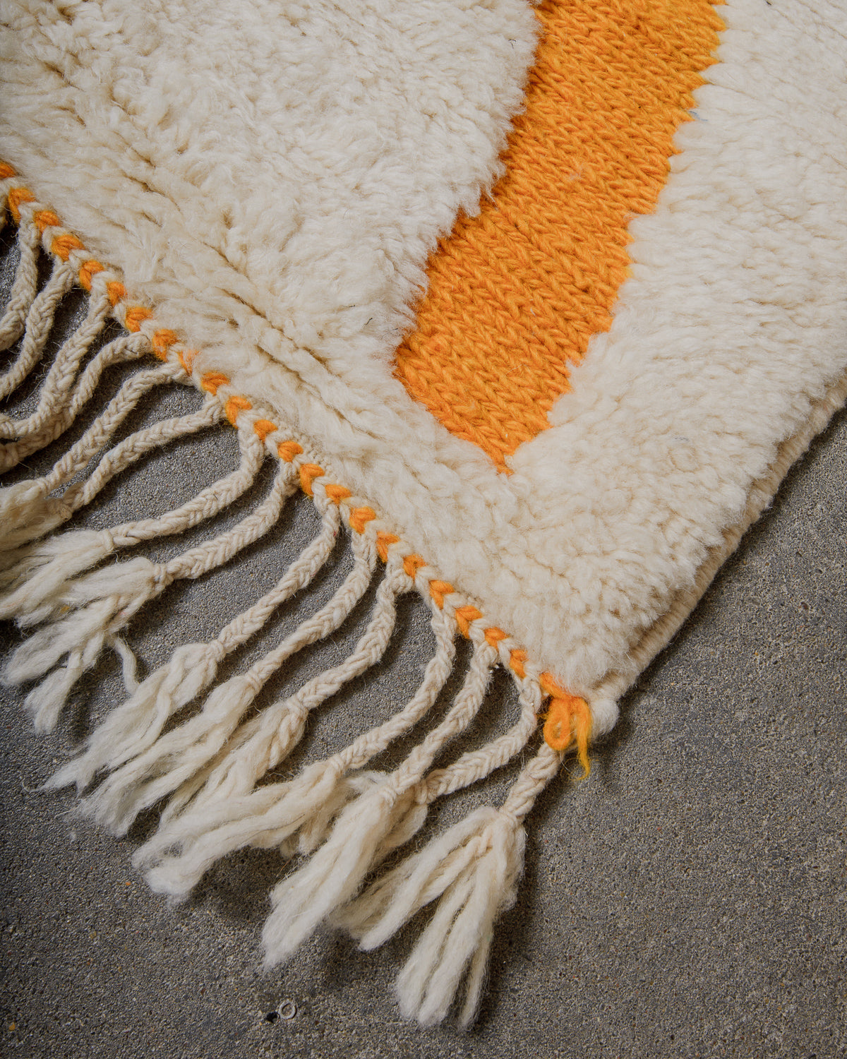 Textured rug with white fringe and saffron woven pattern on a concrete floor.