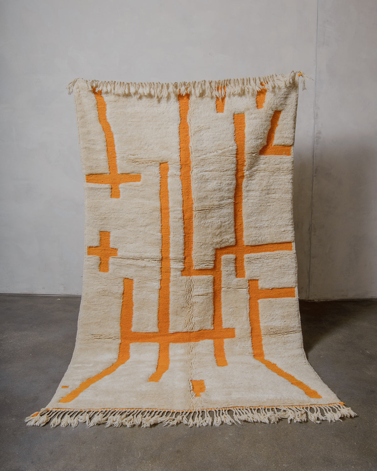 Cream wool Berberlin Finest rug with saffron yellow geometric patterns held up in front of a white wall.