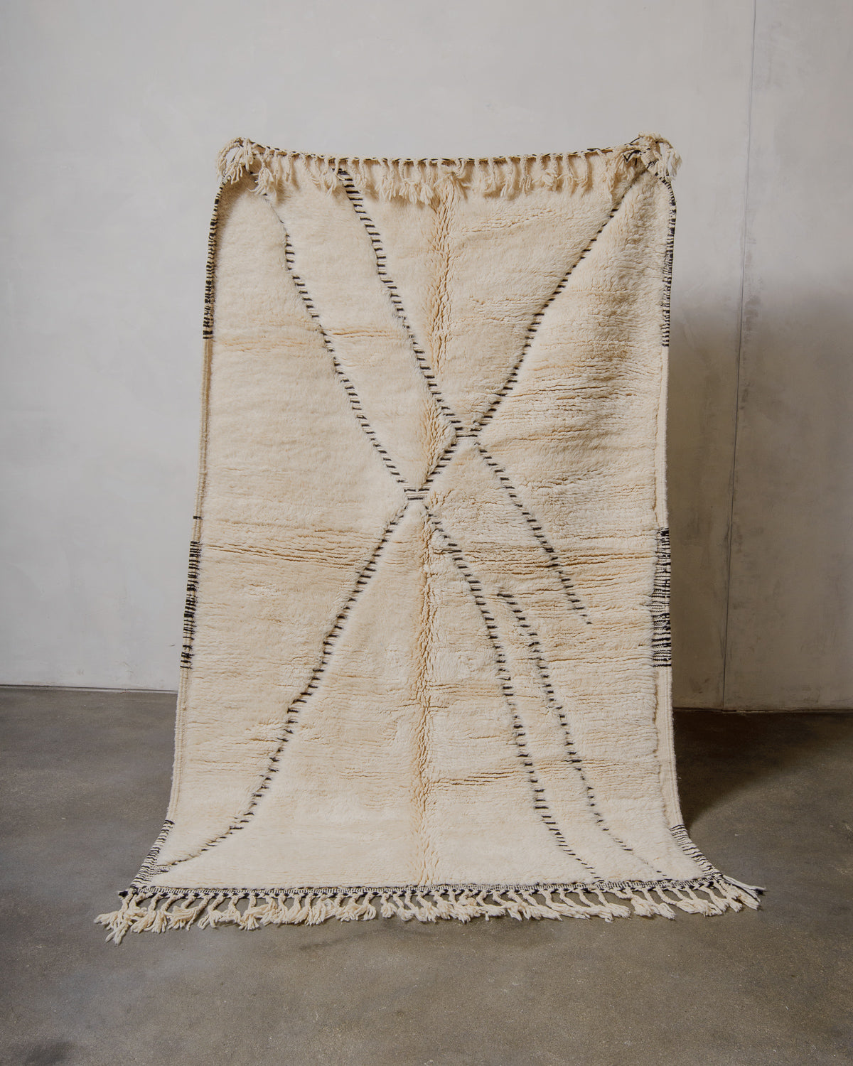Cream wool rug with black design and fringes on a plain background