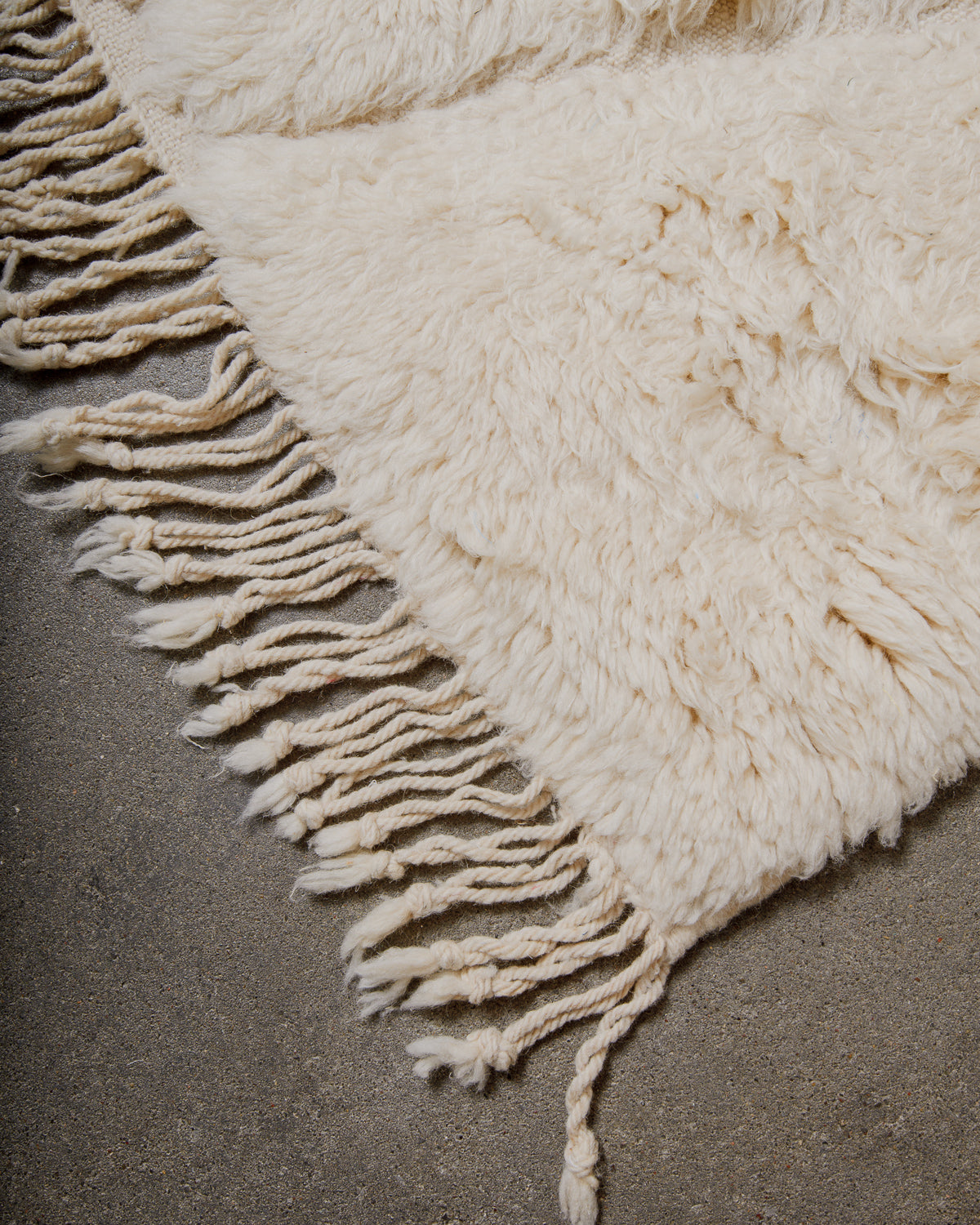 Close-up of a fluffy cream rug with fringes on a dark surface.