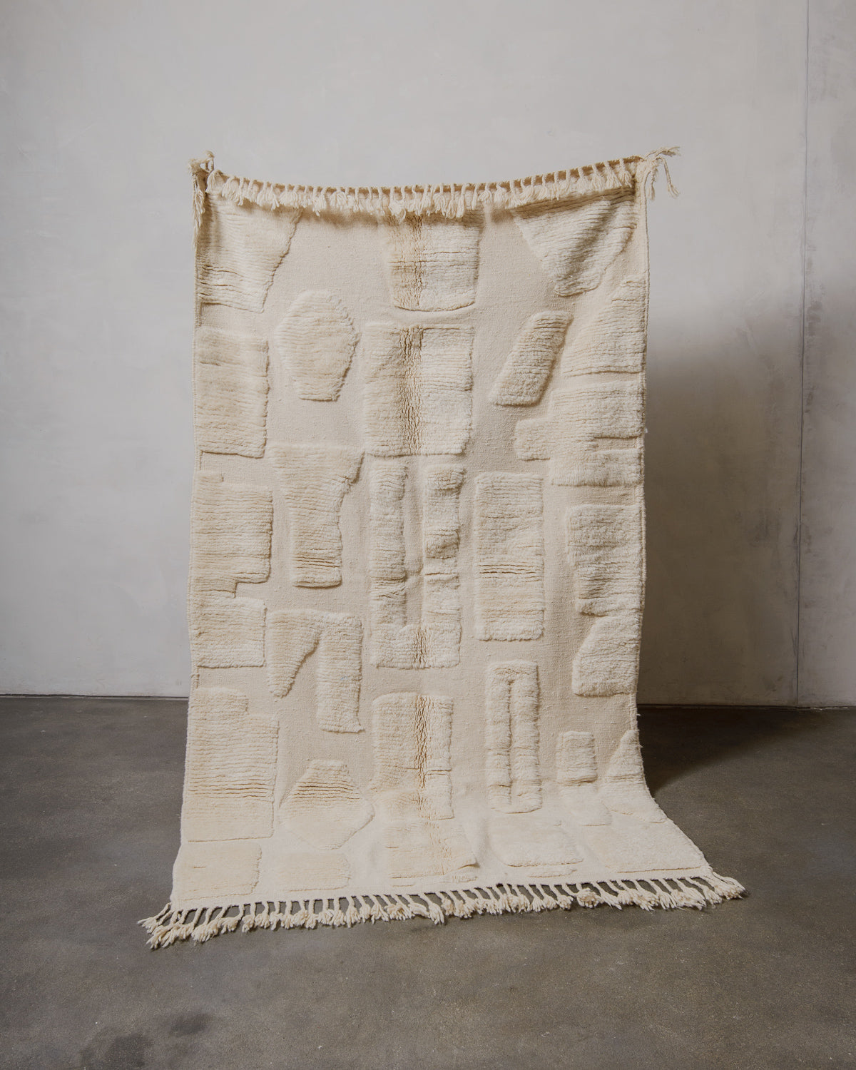 Textured beige rug held up against a plain wall.