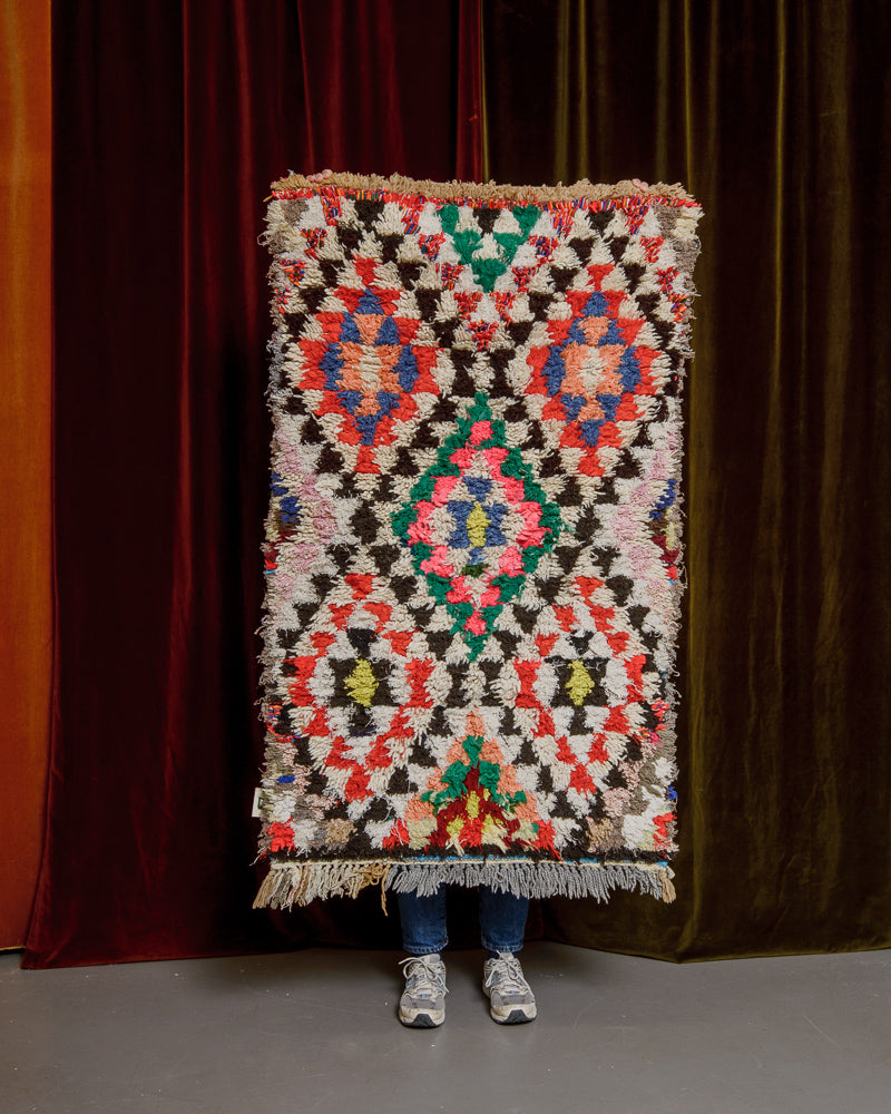 Vintage Berberlin boucherouite runner rug being held up in front of a velvet curtain. 