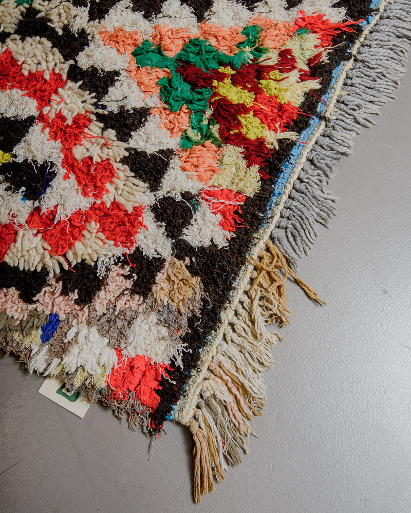 Corner of boucherouite rug with red, green, yellow, black and white yarn and fabric remnants, cream wool and with short fringe.