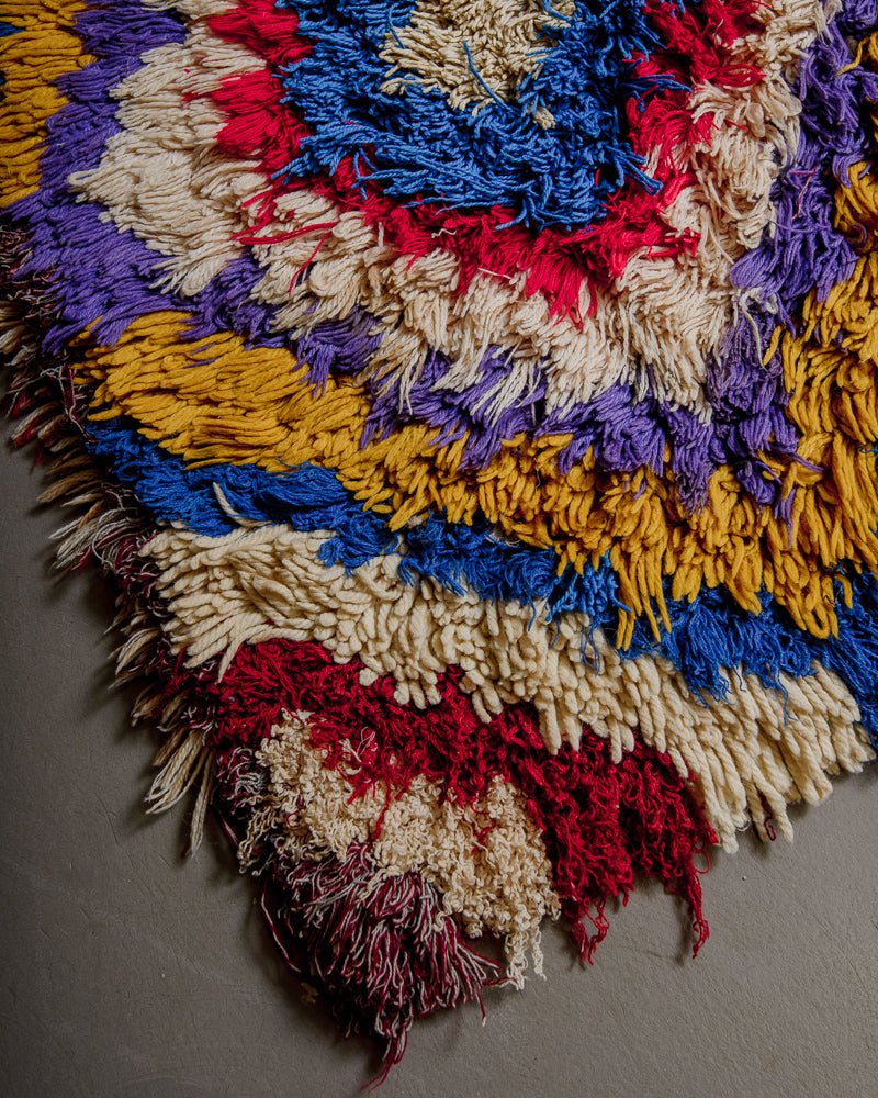 Corner of boucherouite rug with red, yellow, purple, blue and white cotton .