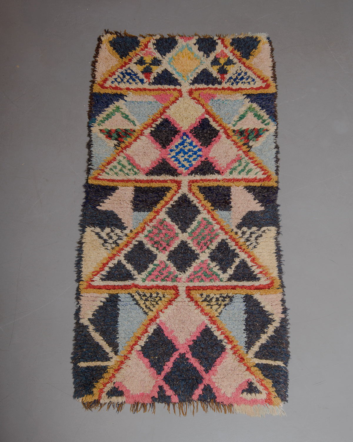 Vintage Berberlin boucherouite runner rug on grey floor in front of velvet curtain. 